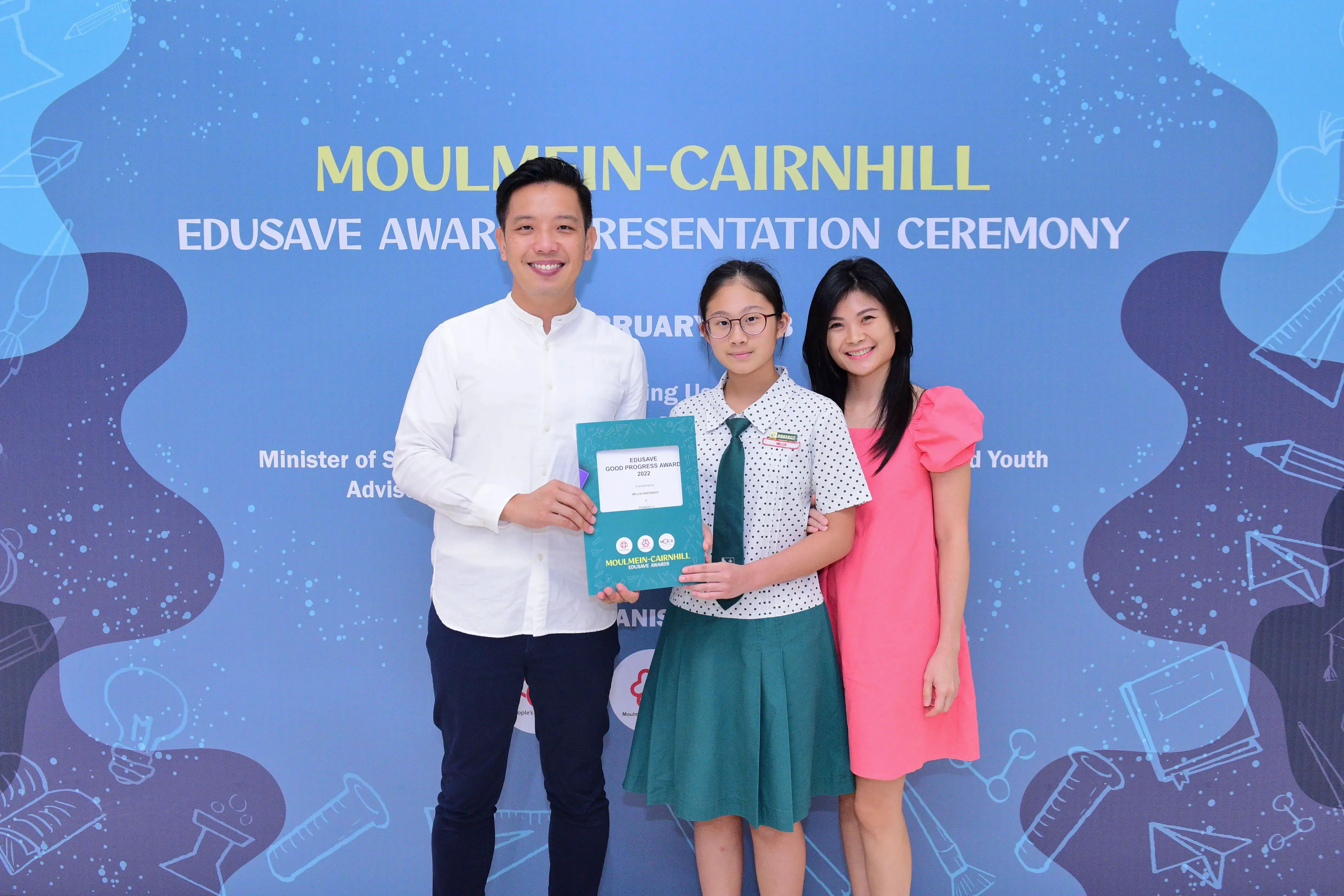 Three people pose at the Moulmein-Cairnhill Edusave Award Presentation Ceremony, with a student holding a certificate.