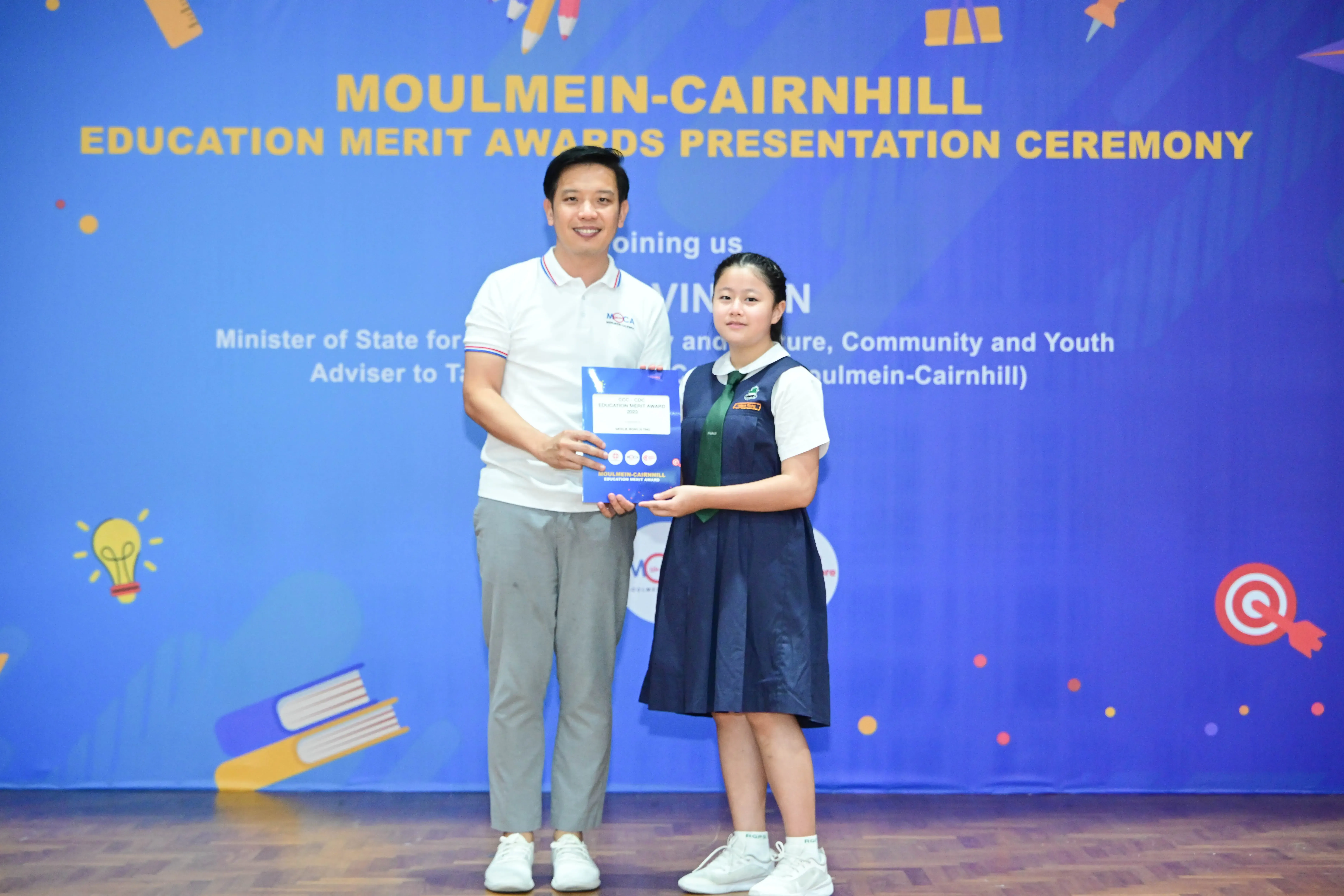 A man and a uniformed schoolgirl hold an award together at the Moulmein-Cairnhill Education Merit Awards ceremony.
