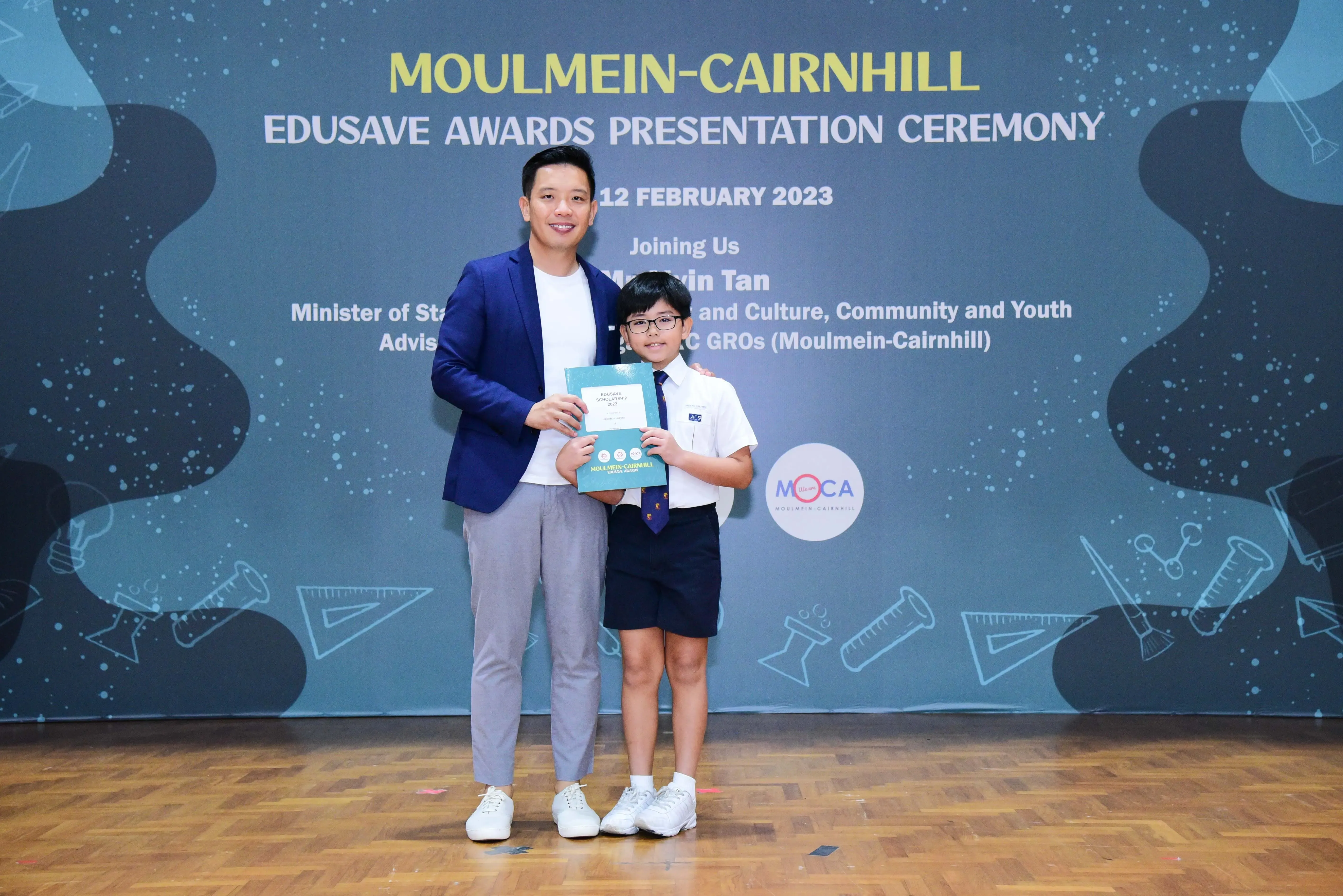 Man in blue blazer and young boy in school uniform hold an award at Moulmein-Cairnhill Edusave Awards Ceremony 2023.