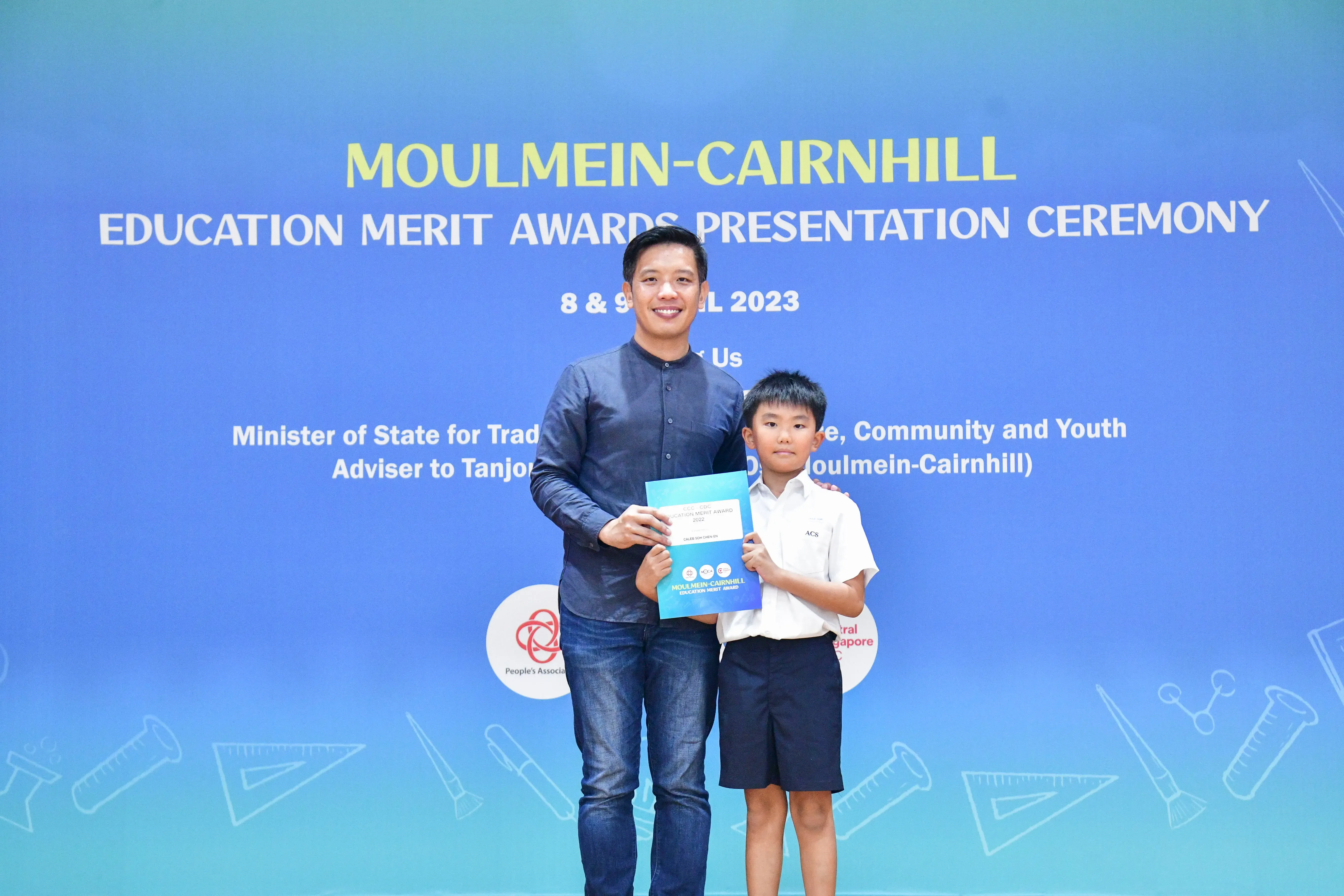 An adult and a young boy in school uniform hold a certificate at the Moulmein-Cairnhill Education Merit Awards 2023.