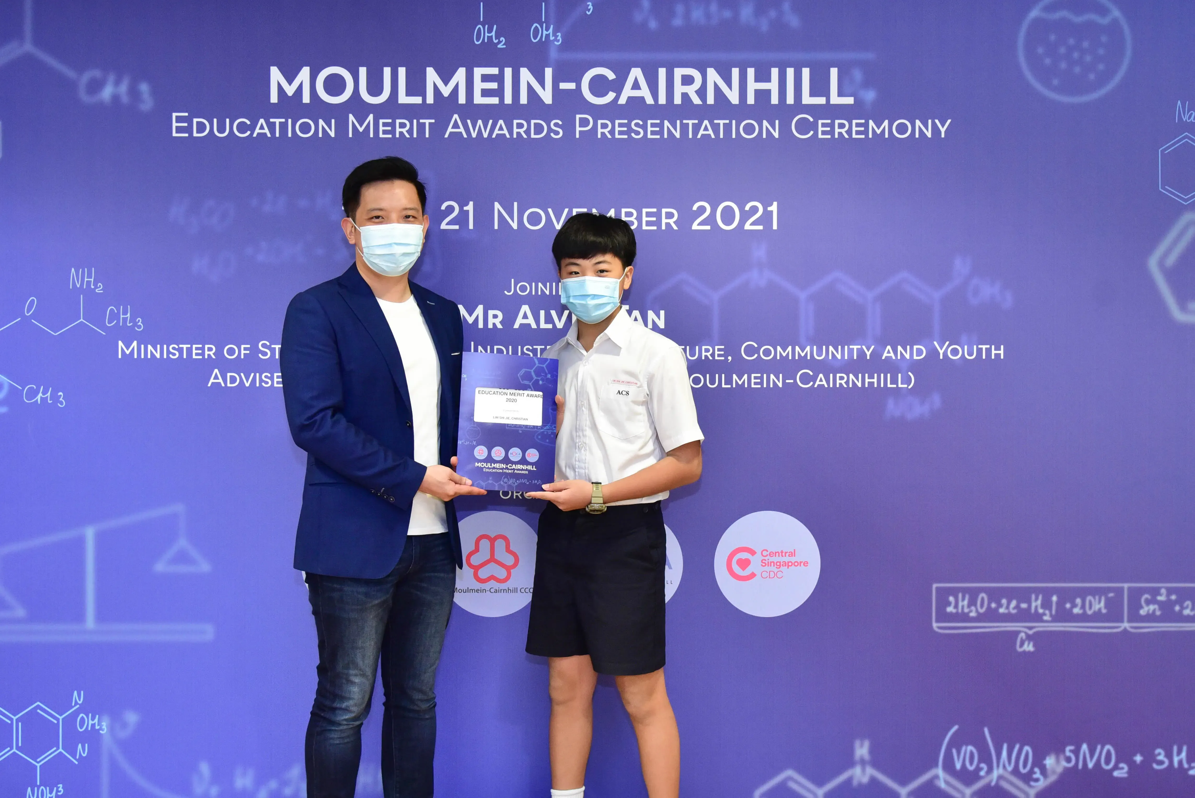 Two masked individuals hold an award certificate at the Moulmein-Cairnhill Education Merit Awards Ceremony, November 2021.