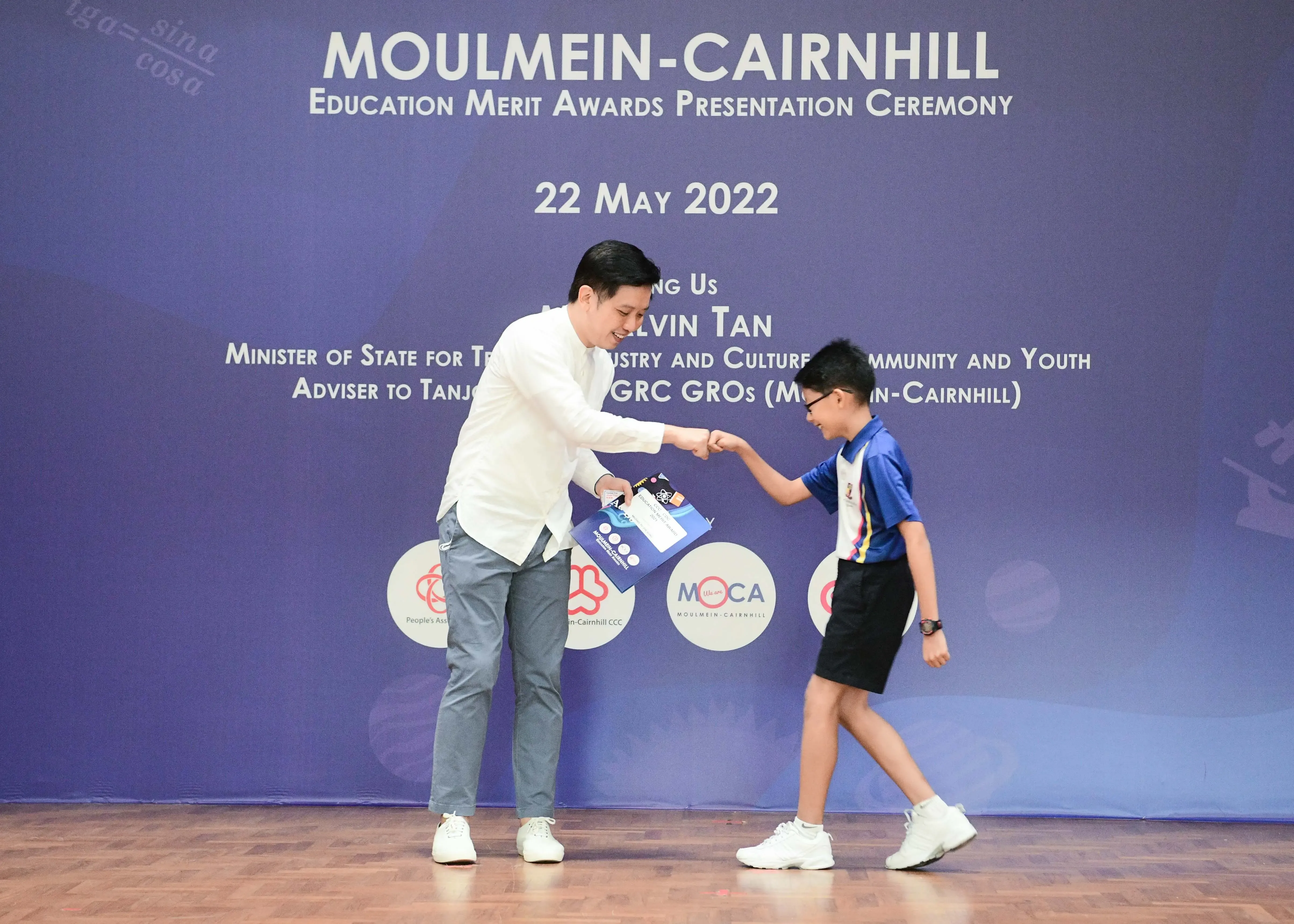 An adult in white shirt fist-bumps a young boy on stage at the Moulmein-Cairnhill Education Merit Awards 2022.