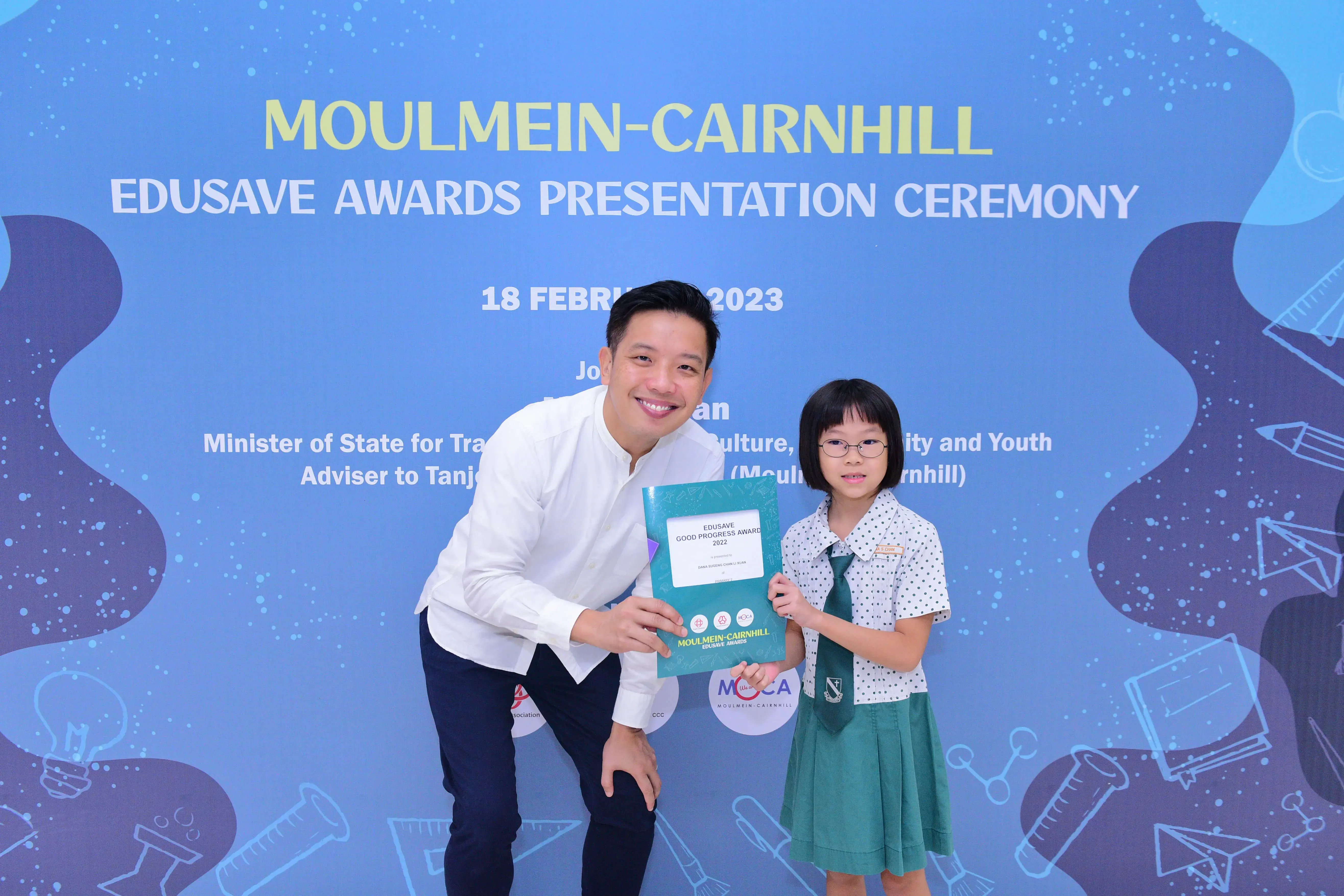 A man and a young girl hold an Edusave award at the Moulmein-Cairnhill Awards Presentation Ceremony 2023.