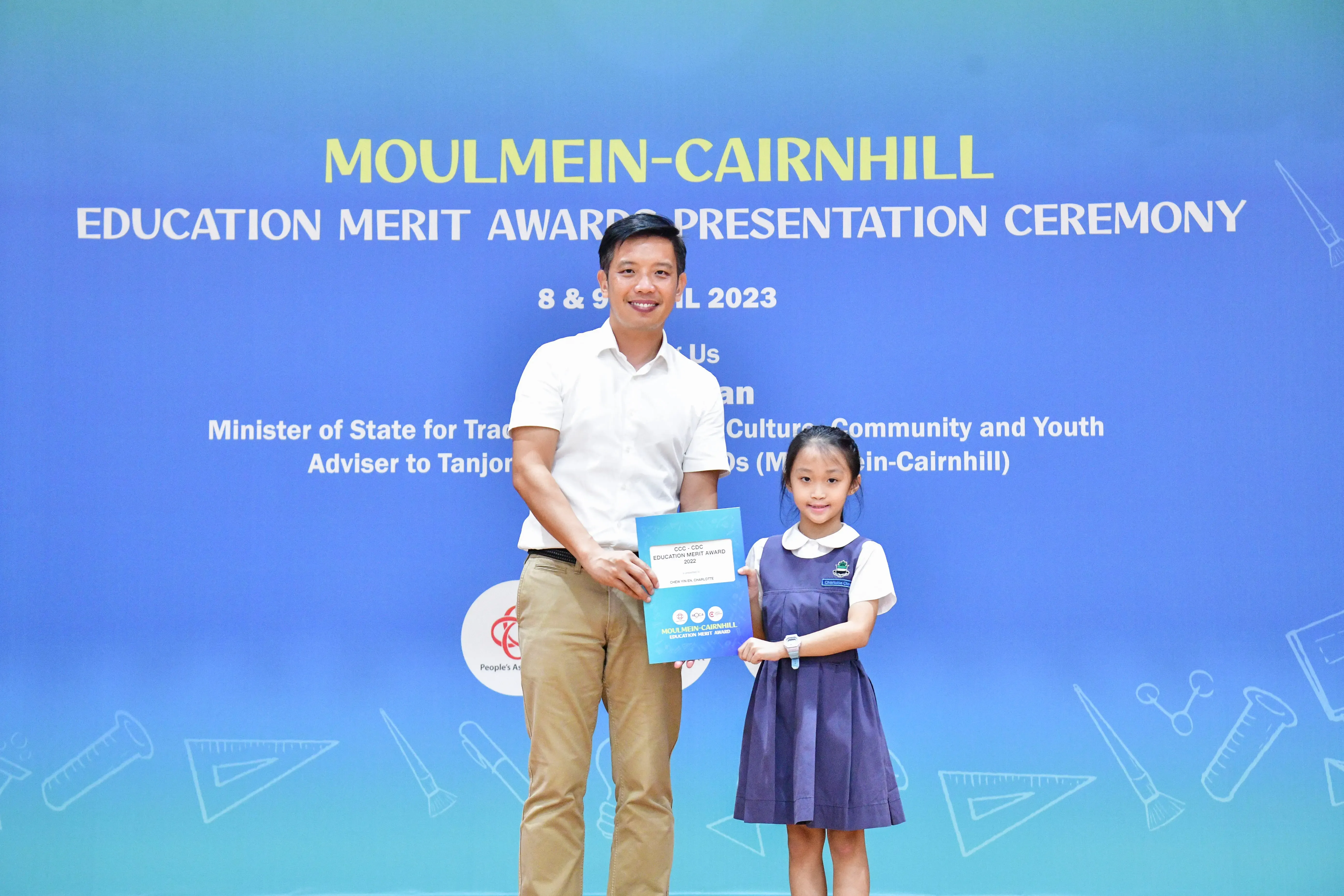 A man and a young girl in school uniform hold an award certificate at the Moulmein-Cairnhill Education Merit Awards 2023.