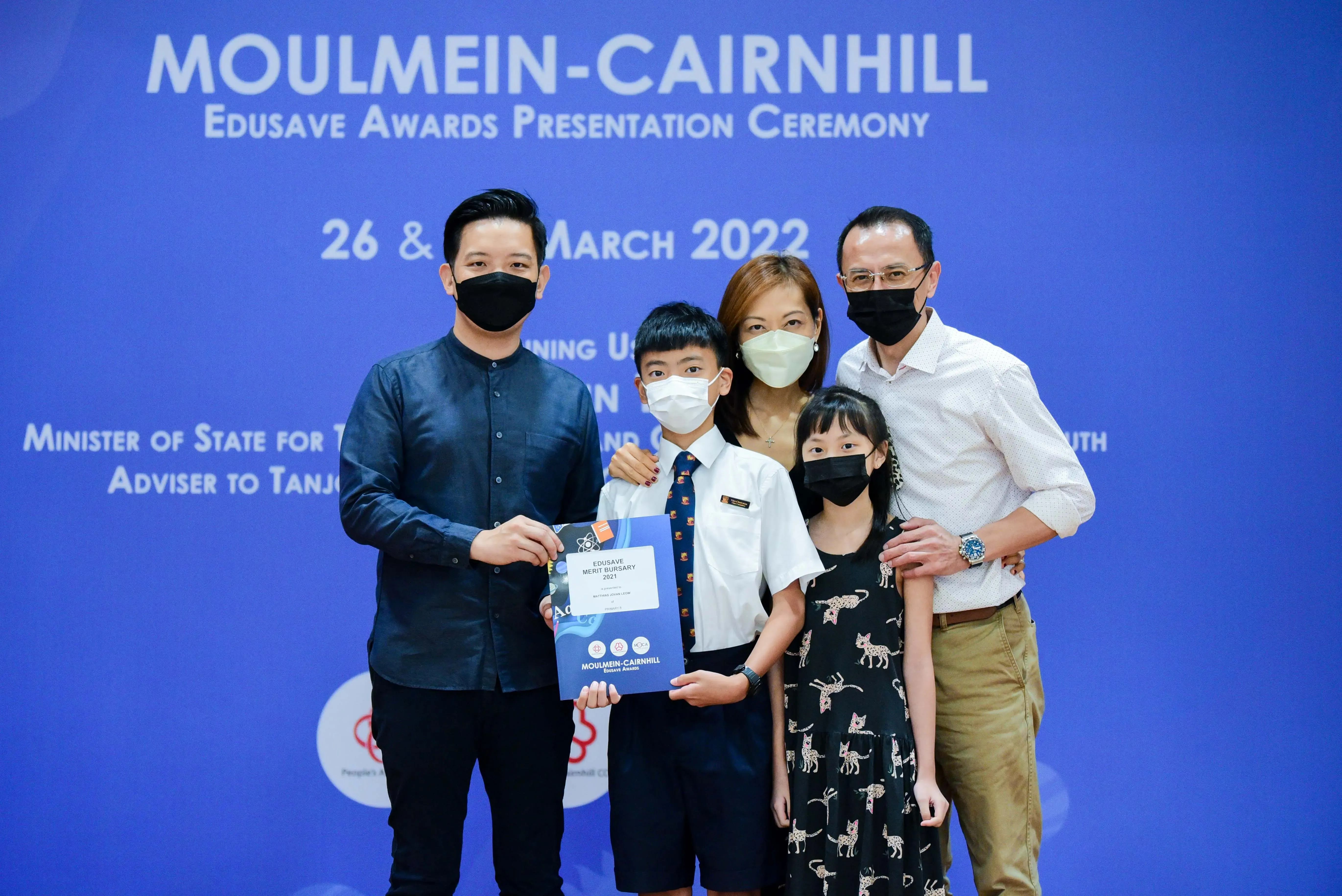 Five masked people pose with an Edusave Merit Bursary 2021 certificate at the Moulmein-Cairnhill Awards Ceremony, March 2022.