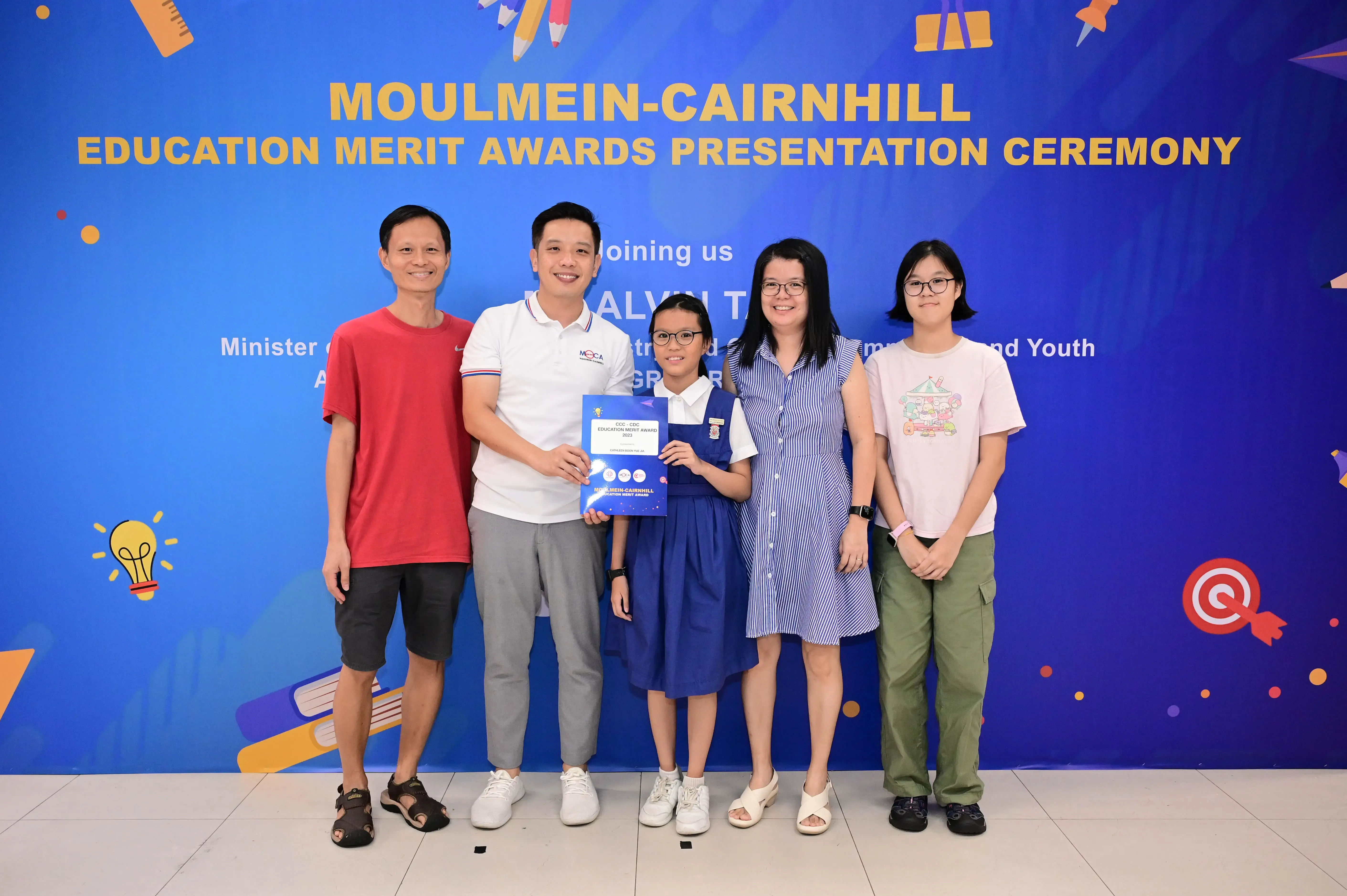 Five people pose at the Moulmein-Cairnhill Education Merit Awards Presentation Ceremony, with a girl holding a blue certificate.