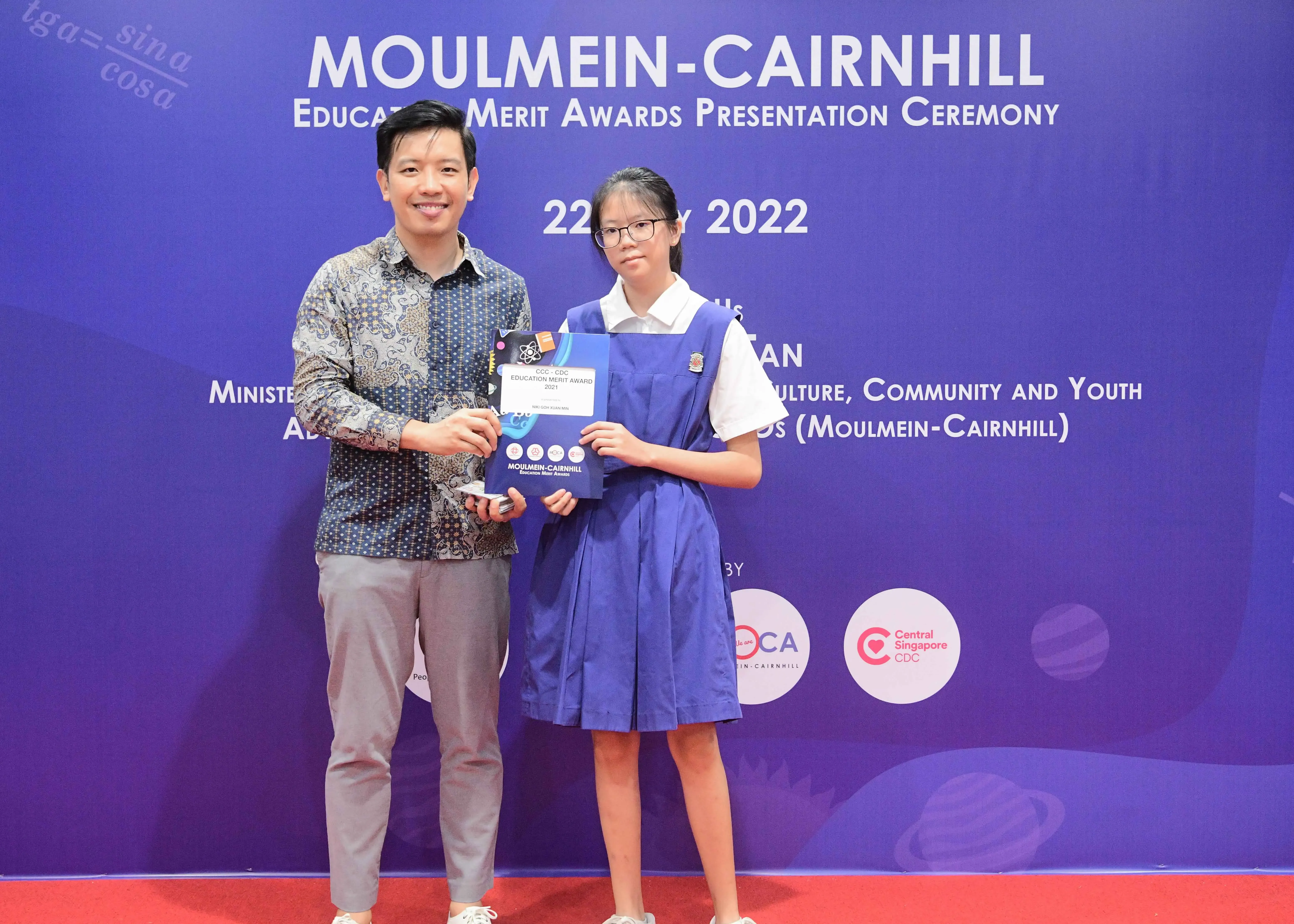 A man and a young girl hold an award certificate at the Moulmein-Cairnhill Education Merit Awards Ceremony 2022.