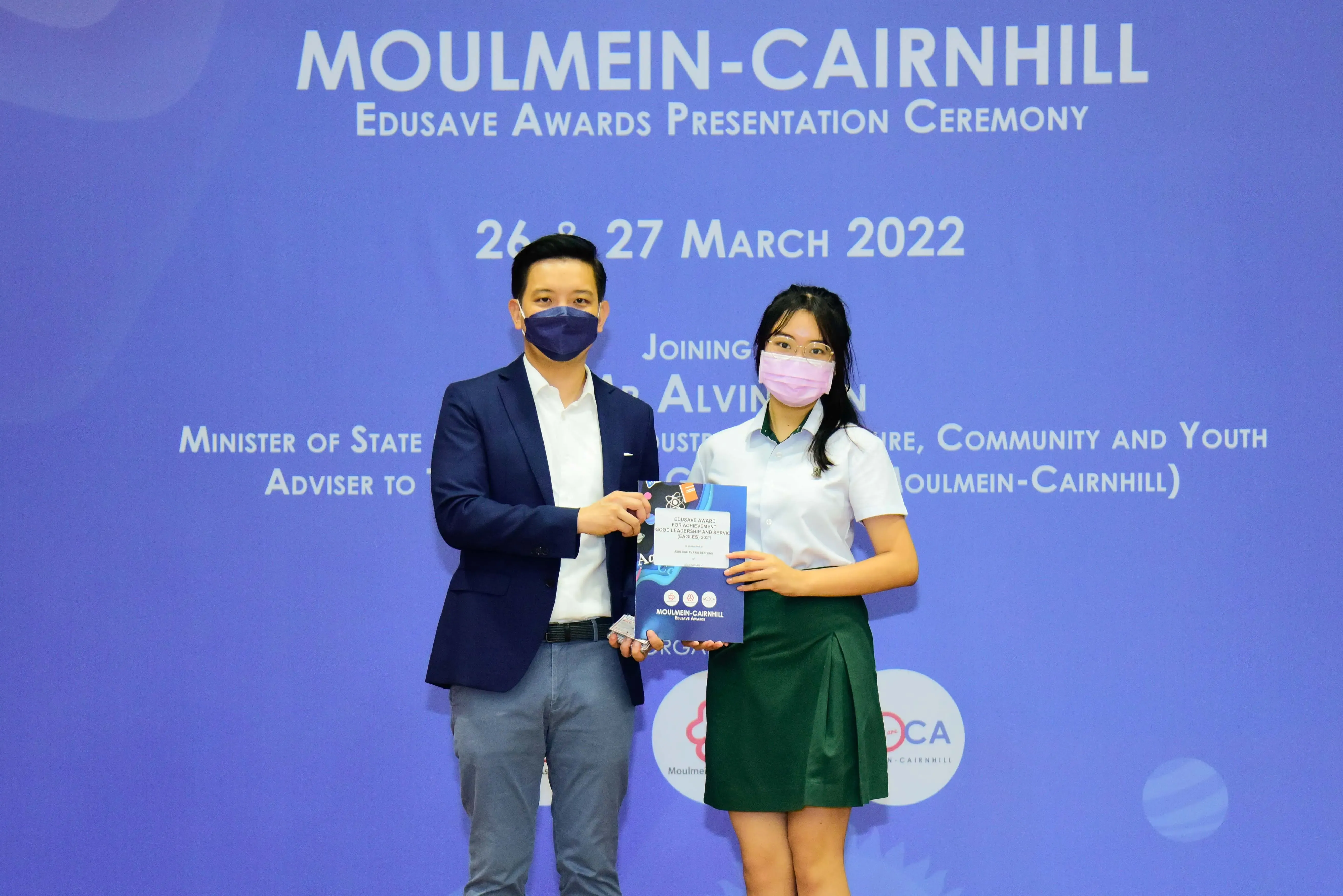 Two masked people hold an award booklet at the Moulmein-Cairnhill Edusave Awards Presentation Ceremony, March 2022.