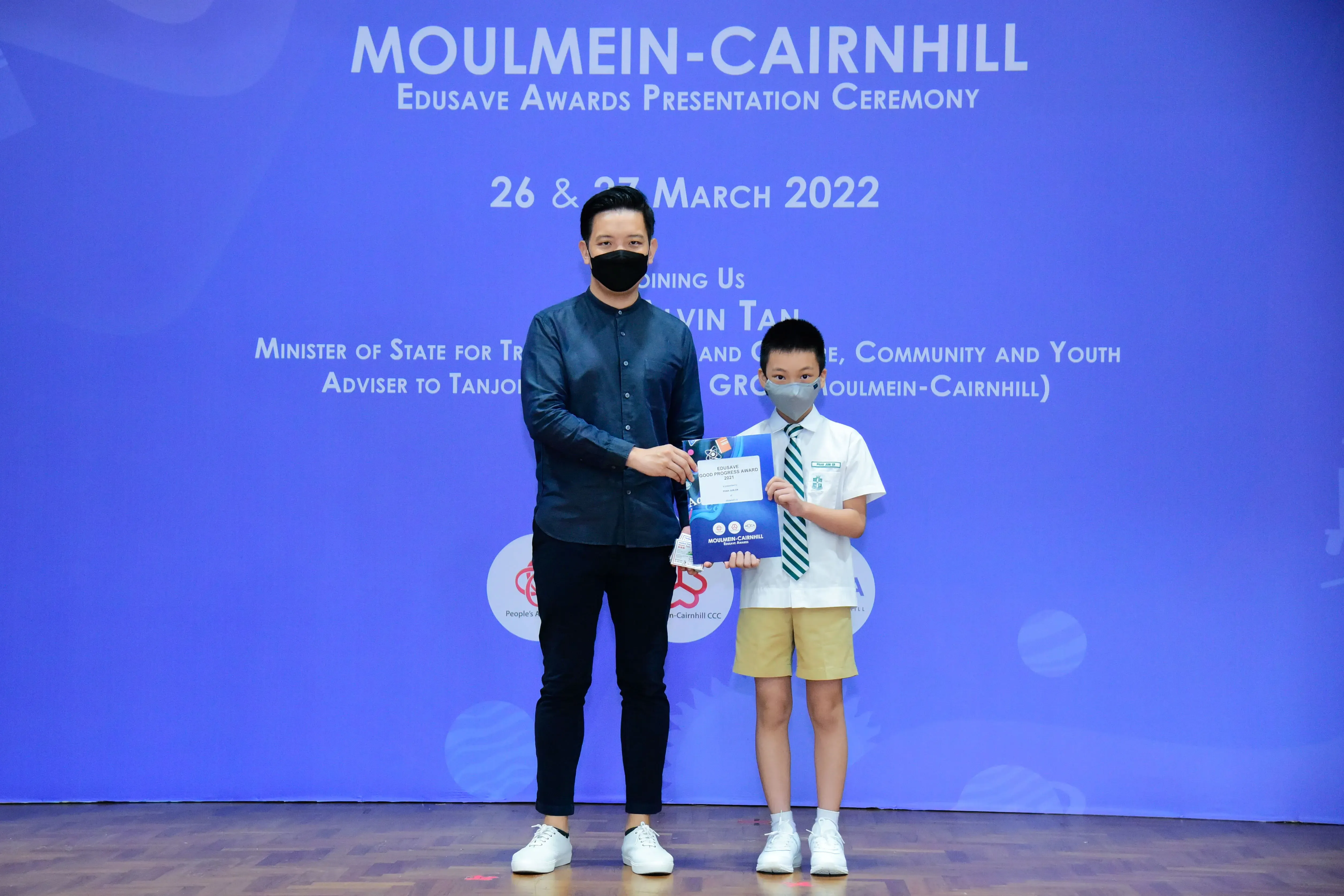 An adult and a young boy in school uniform hold an award at the Moulmein-Cairnhill Edusave Awards Ceremony 2022.