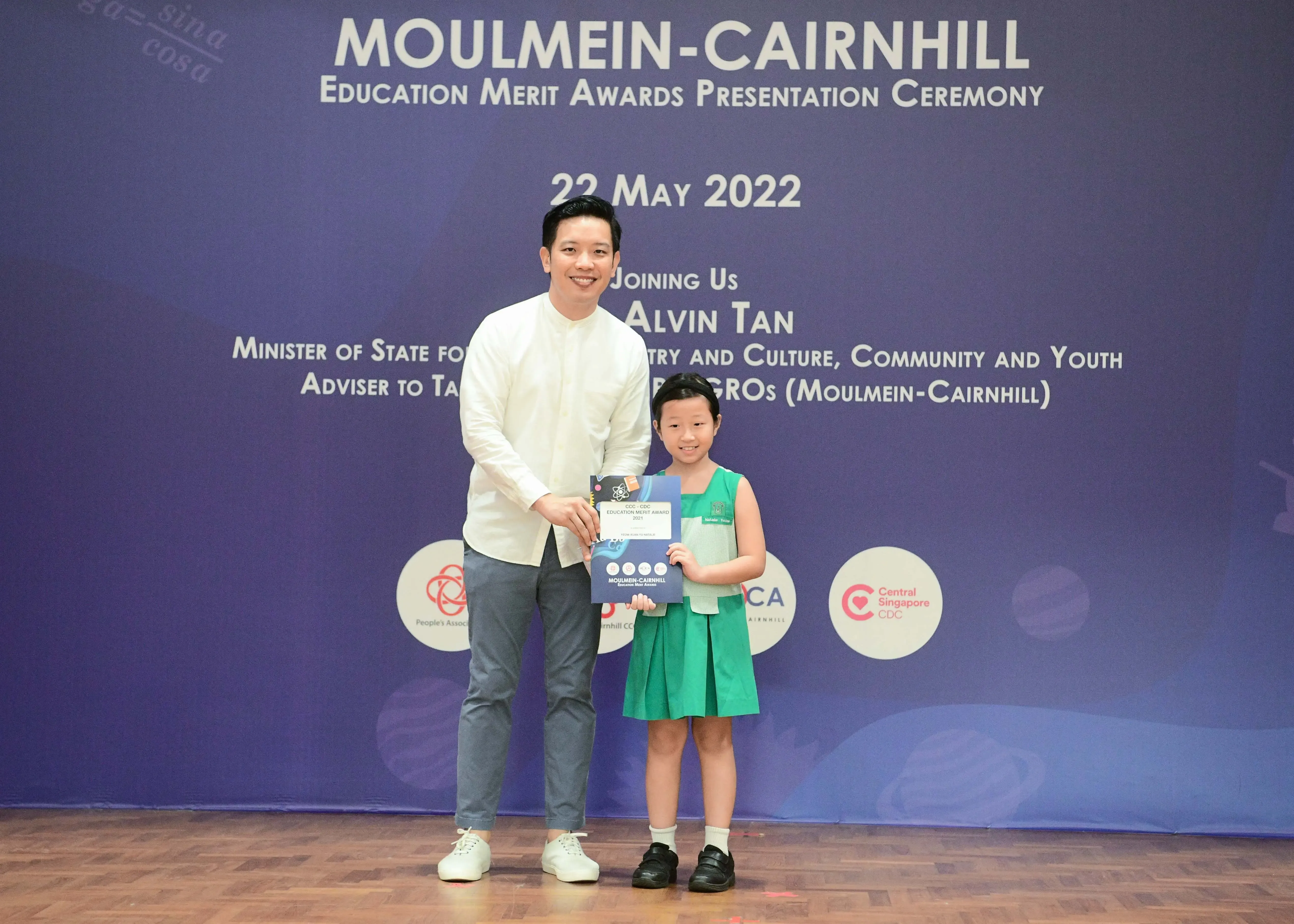 A man and a young girl hold an award certificate at the Moulmein-Cairnhill Education Merit Awards Ceremony on 22 May 2022.