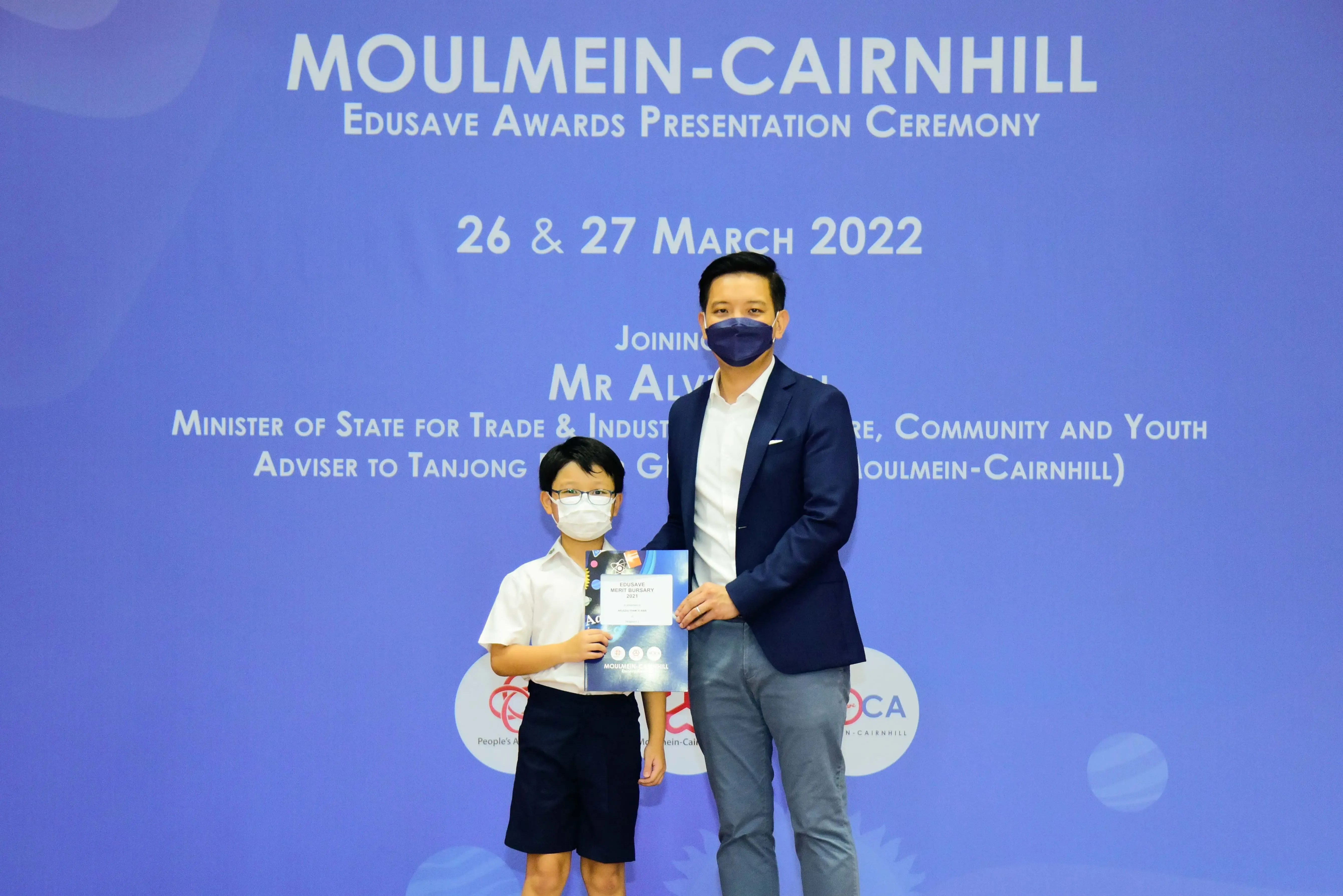 A masked boy and adult man pose at the Moulmein-Cairnhill Edusave Awards Presentation Ceremony on March 2022.