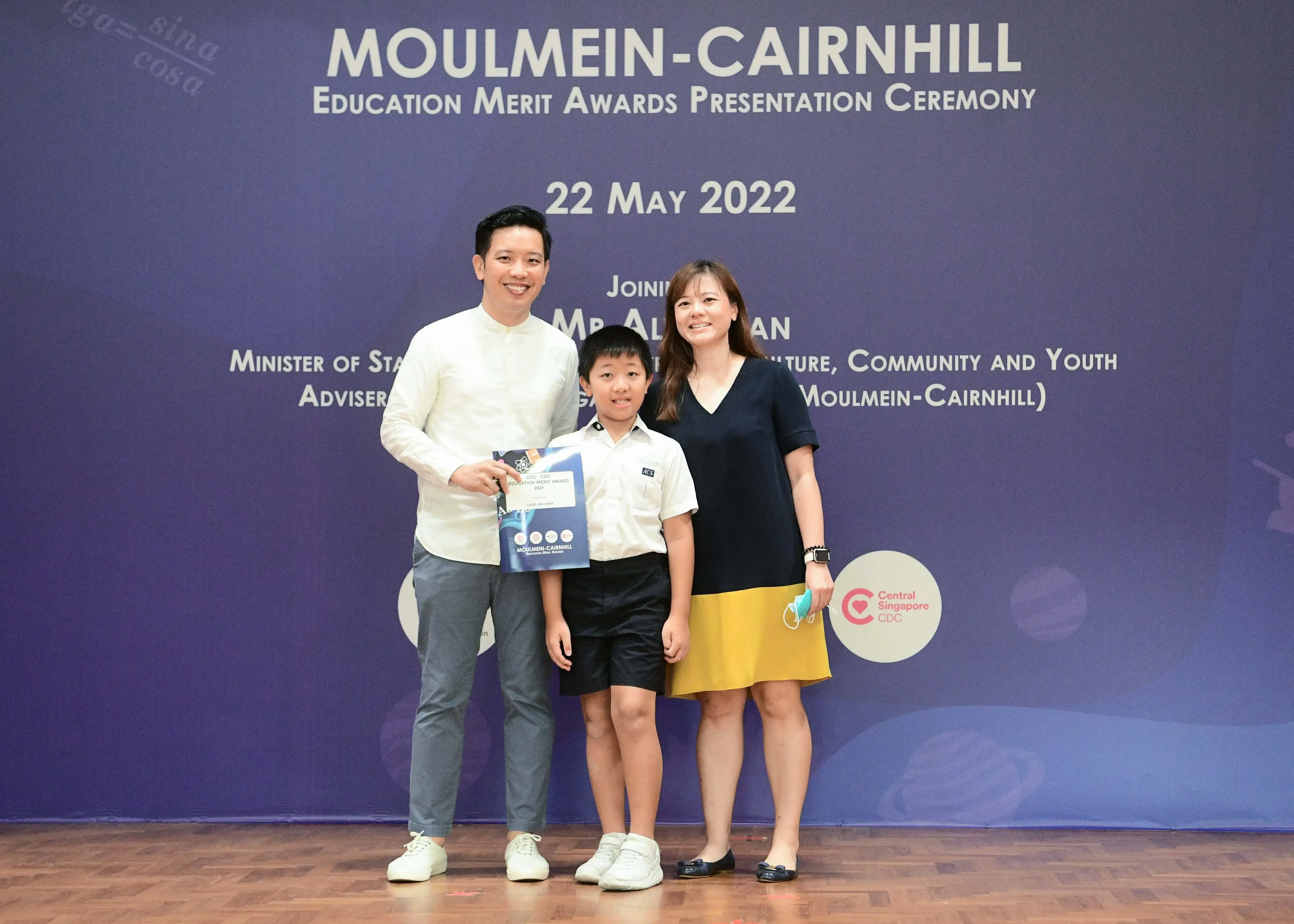 Two adults and a child pose smiling at the Moulmein-Cairnhill Education Merit Awards Ceremony on 22 May 2022.