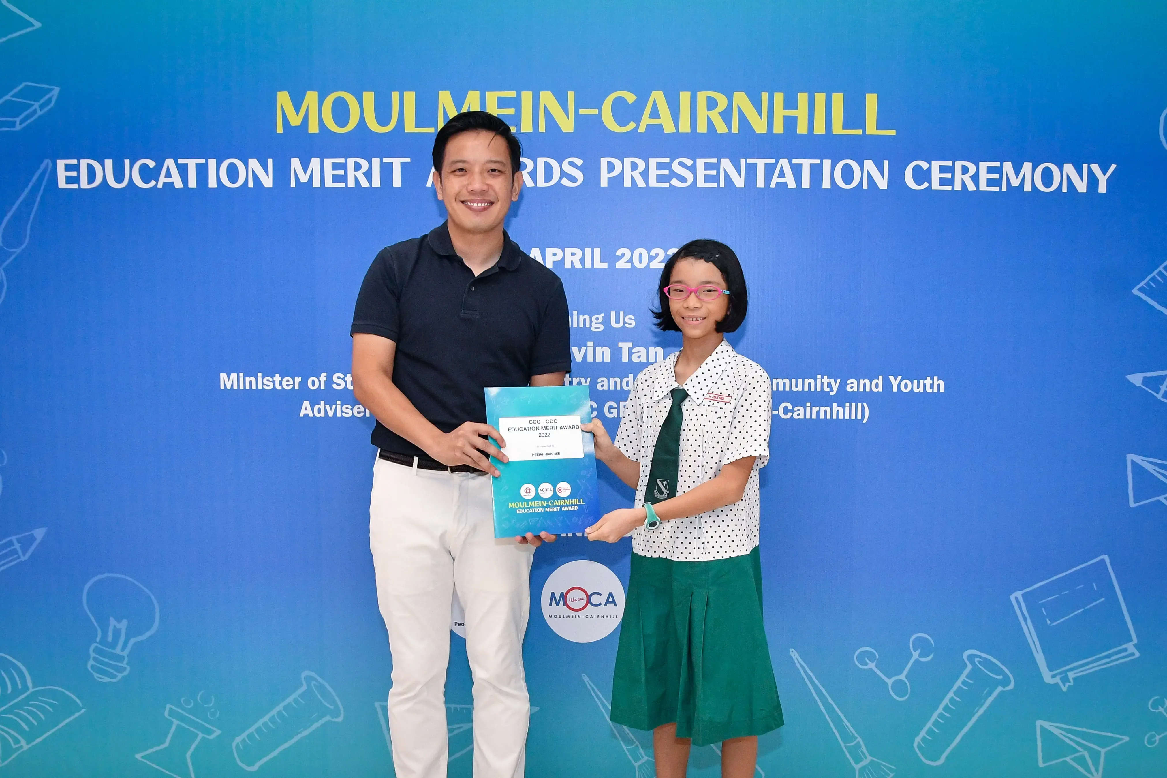 A man and a young girl hold an award certificate at the Moulmein-Cairnhill Education Merit Awards Presentation Ceremony.