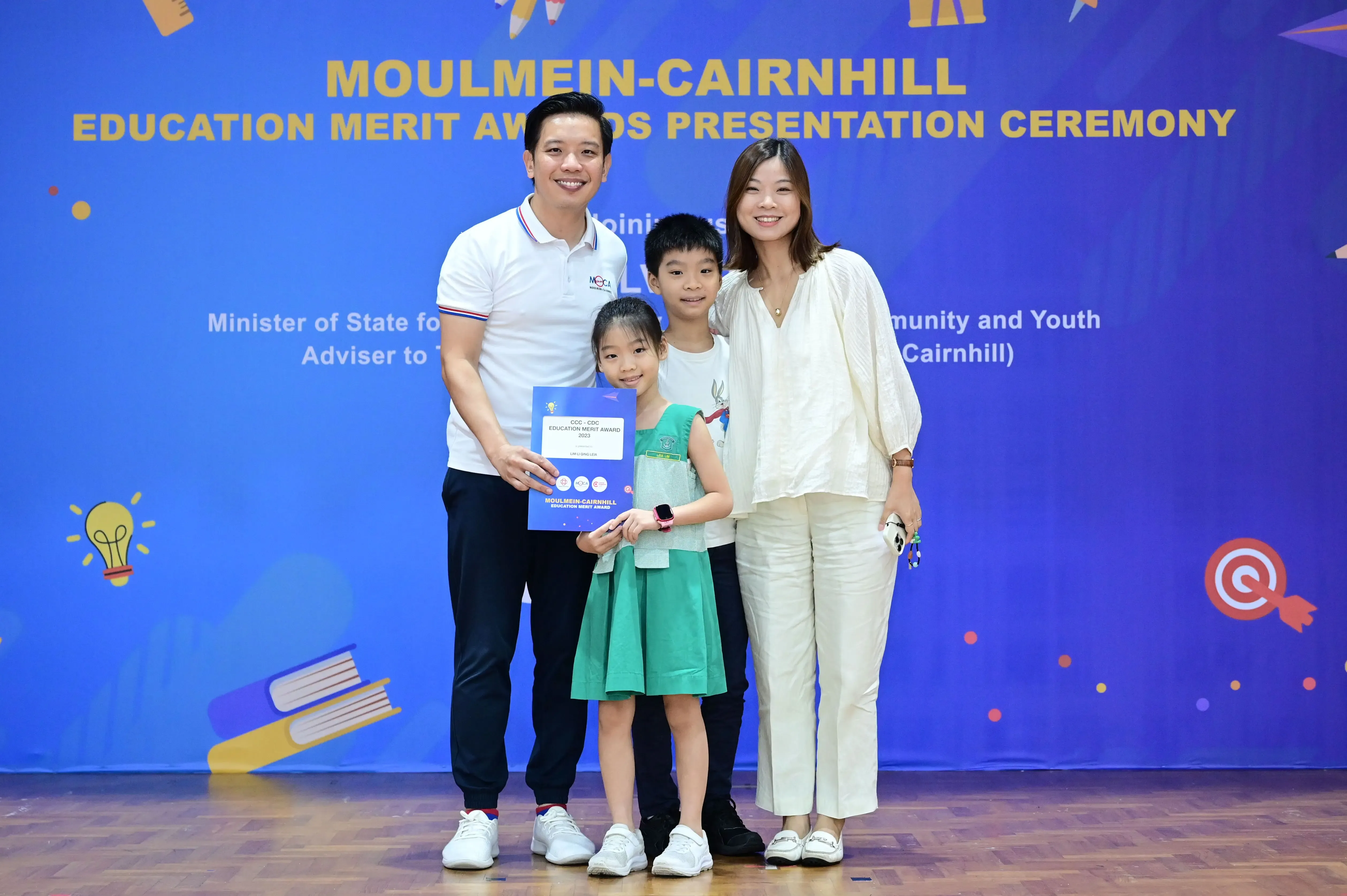 Family of four posing with an award certificate at the Moulmein-Cairnhill Education Merit Awards Presentation Ceremony.