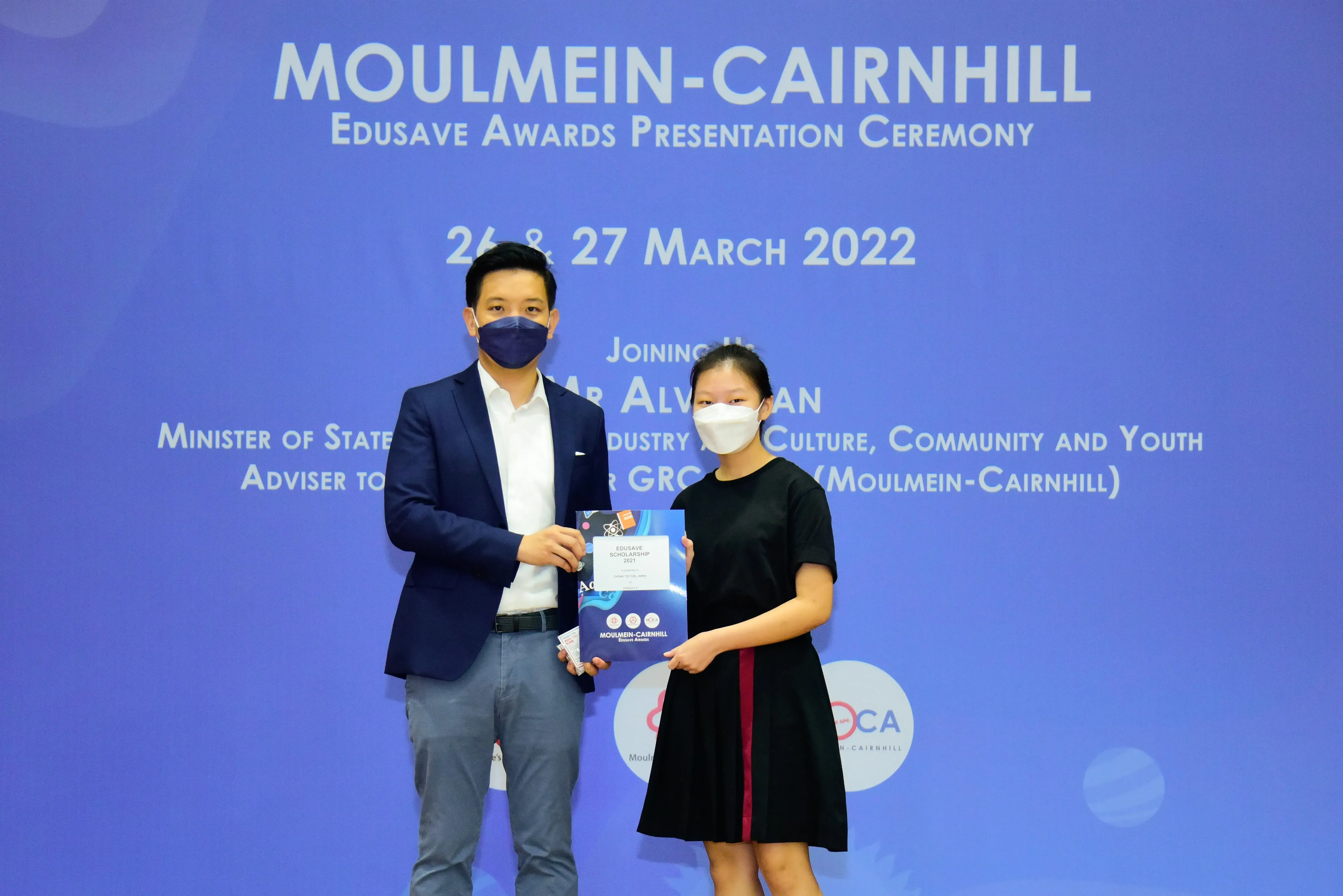 Two masked individuals hold an award booklet at the Moulmein-Cairnhill Edusave Awards Ceremony, March 2022.