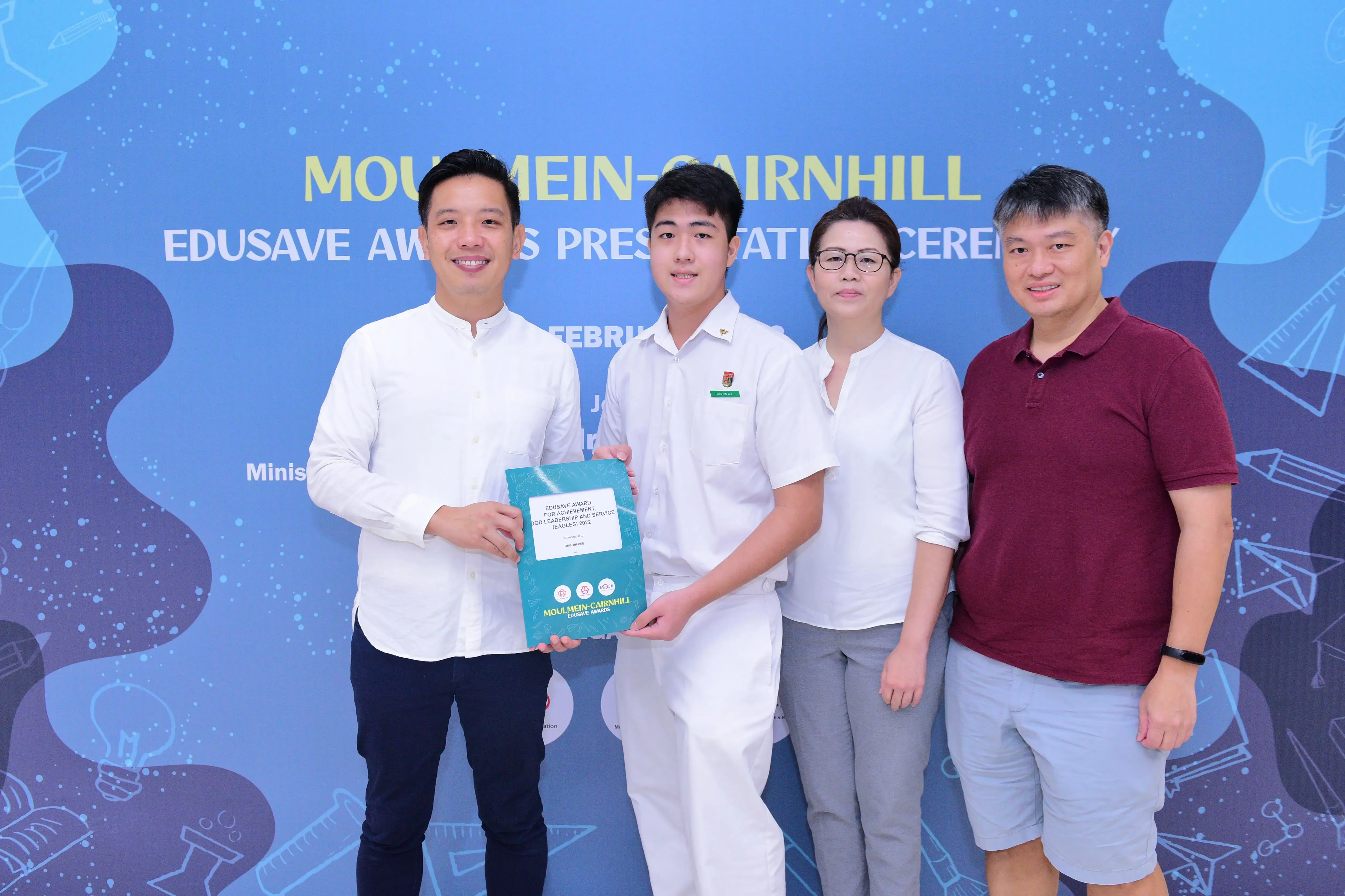 Four people pose at the Moulmein-Cairnhill Edusave Awards Presentation Ceremony, with a student holding a teal award folder.