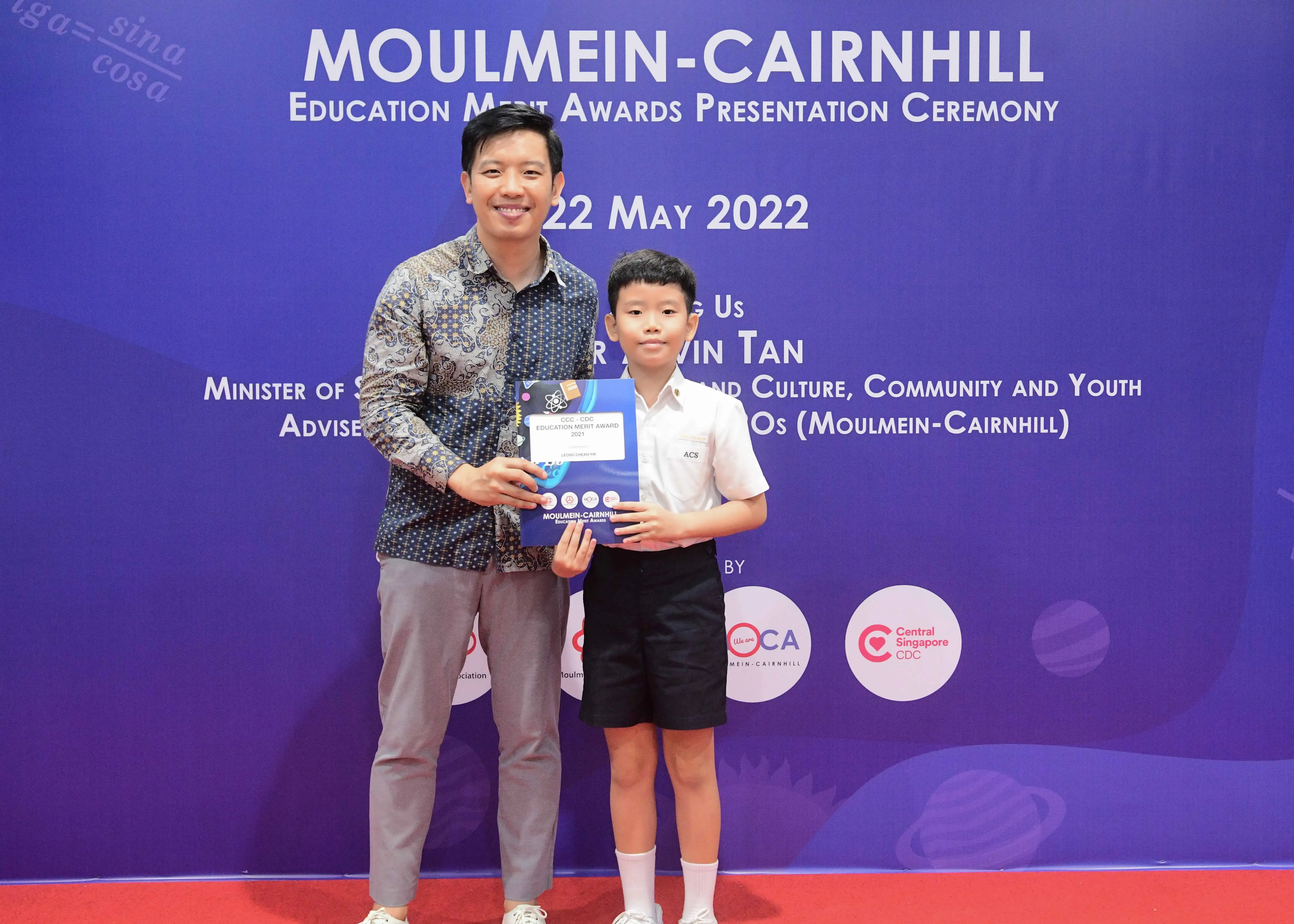 A man and a young boy hold an award certificate at the Moulmein-Cairnhill Education Merit Awards Ceremony, May 2022.