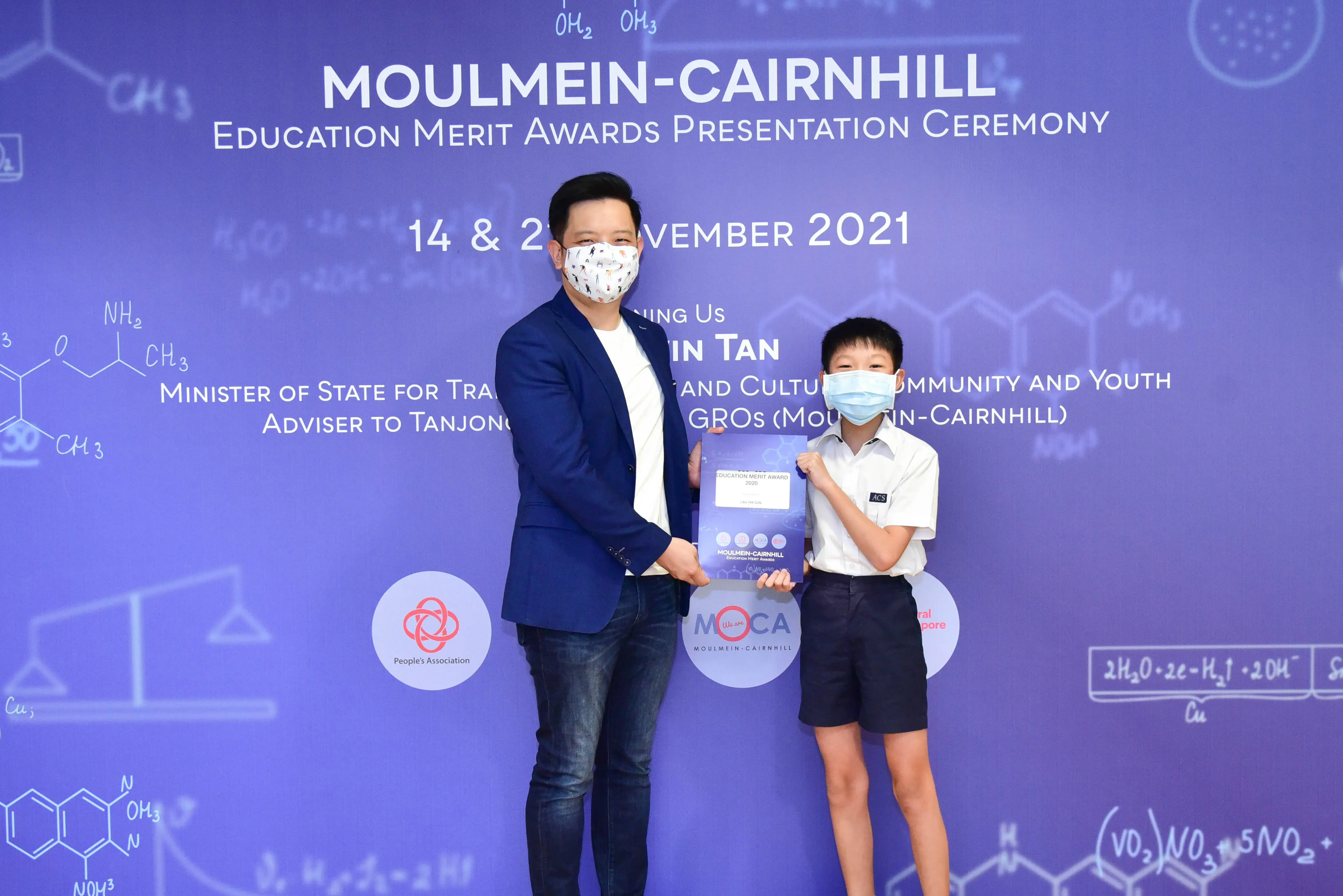 An adult and a young boy wearing masks hold a certificate at the Moulmein-Cairnhill Education Merit Awards 2021.