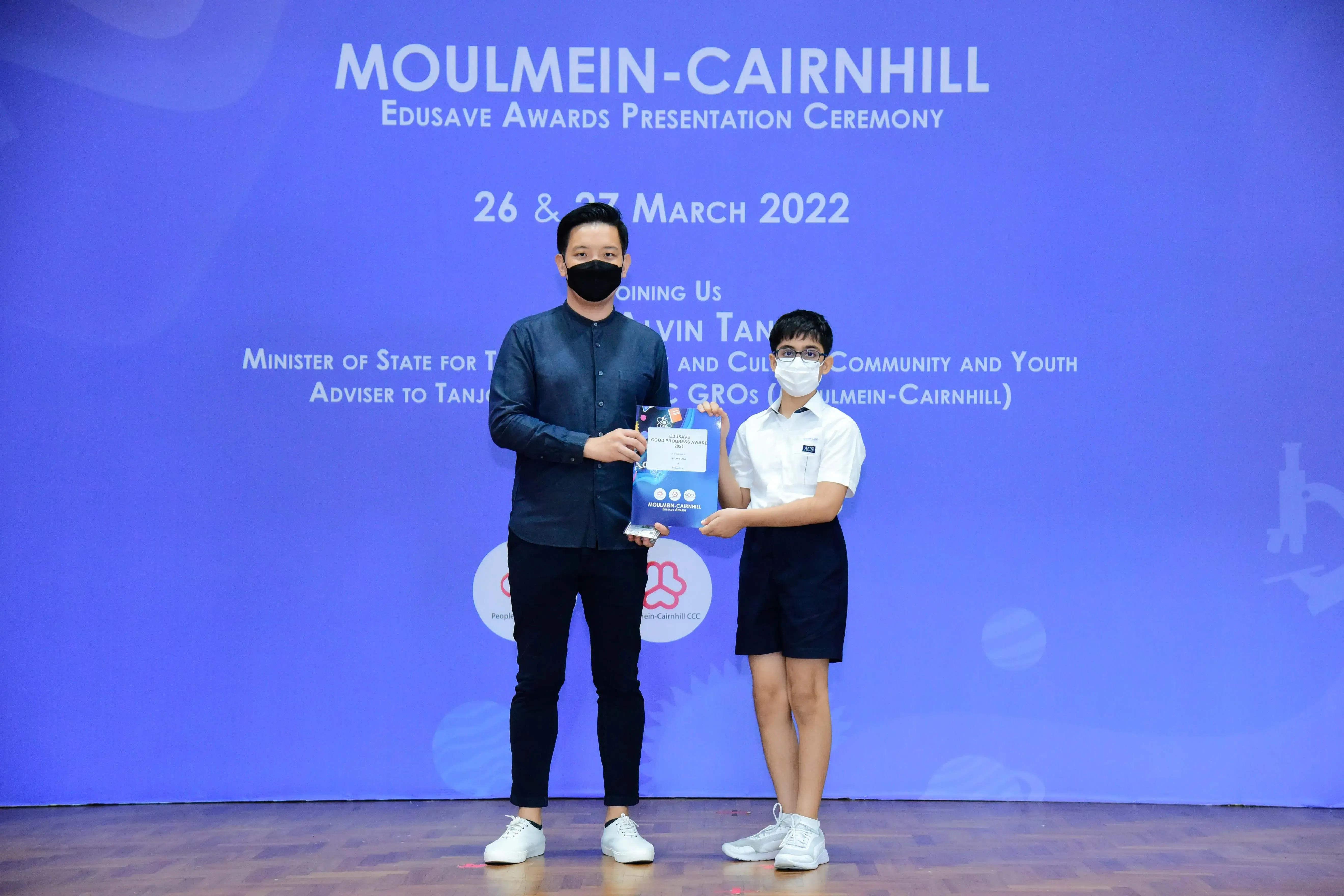 Two masked individuals hold an award at the Moulmein-Cairnhill Edusave Awards Presentation Ceremony, March 2022.