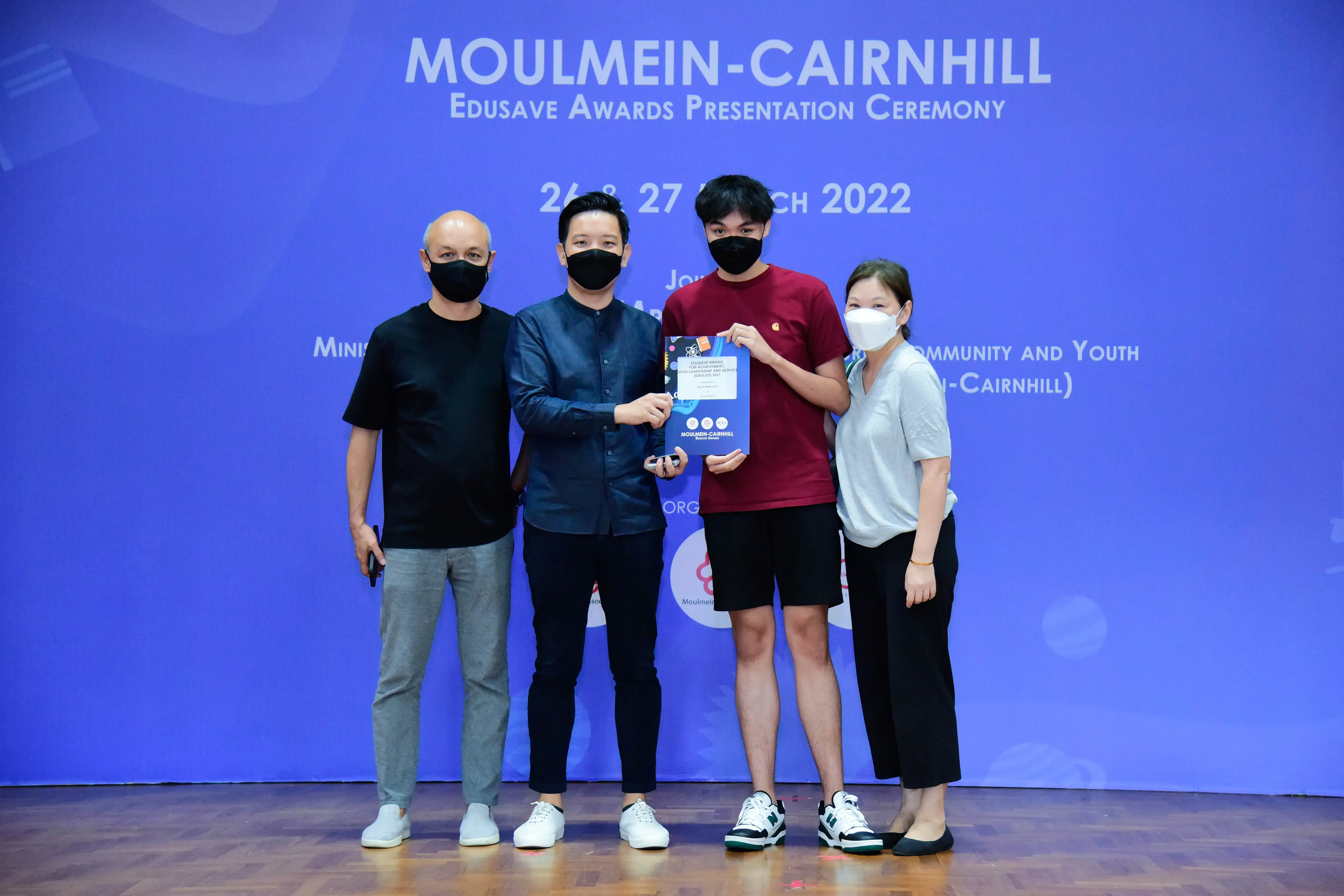 Four masked people pose on stage at the Moulmein-Cairnhill Edusave Awards Presentation Ceremony in March 2022.
