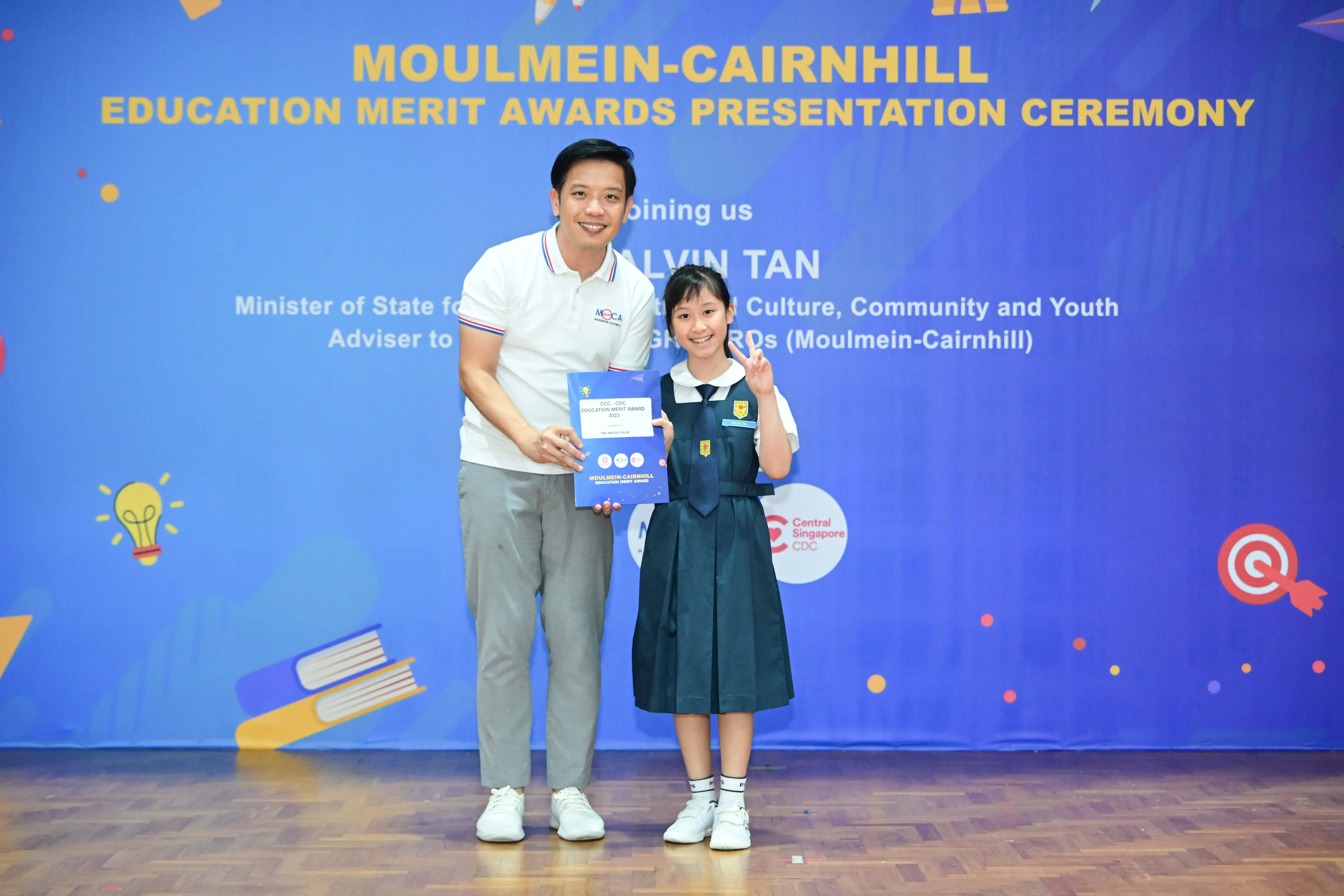 A man and a young girl in school uniform pose with an award certificate at the Moulmein-Cairnhill Education Merit Awards ceremony.