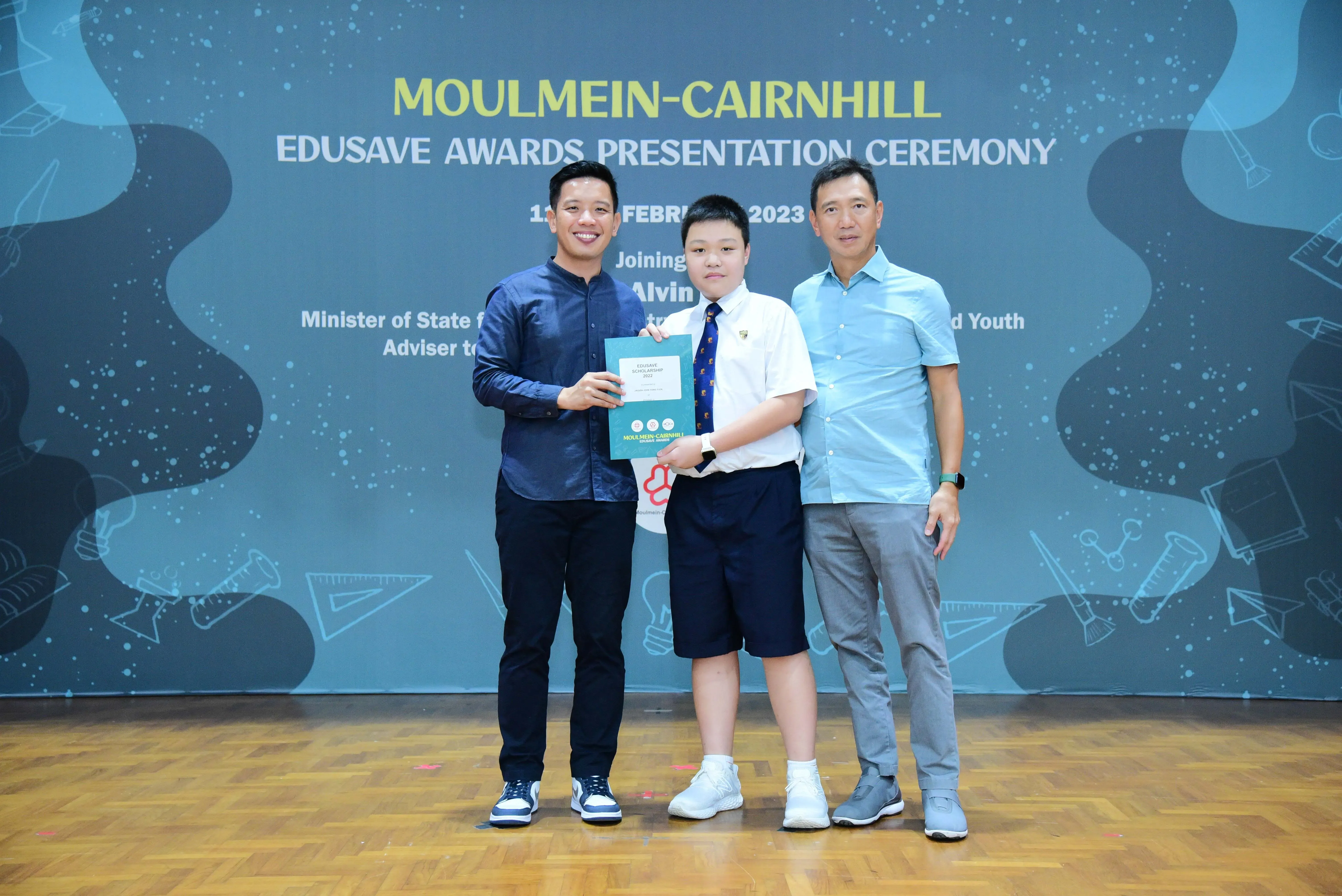 Three people pose at the Moulmein-Cairnhill Edusave Awards Presentation Ceremony, with a student holding a certificate.