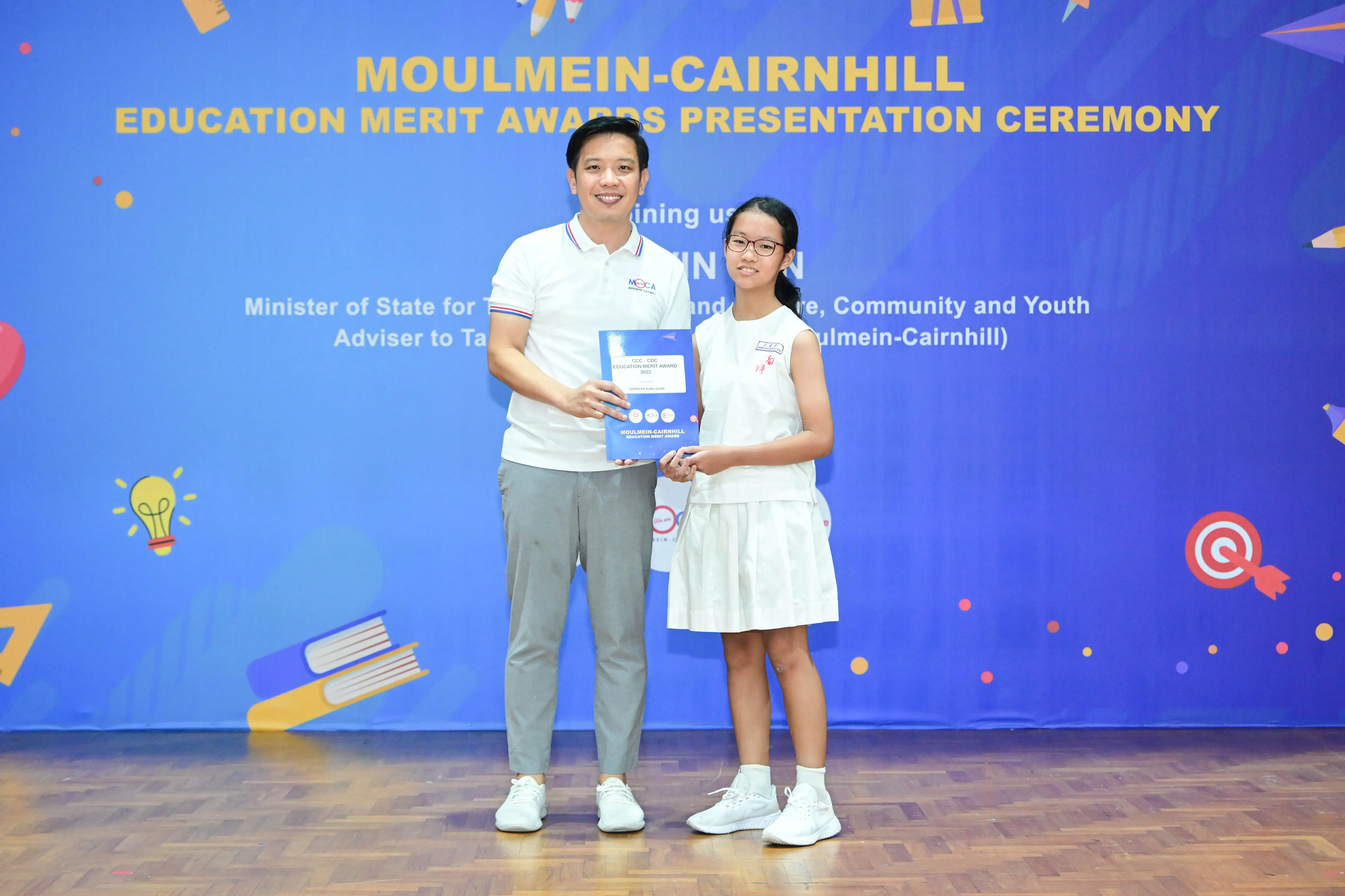 A man and a young girl hold an award certificate at the Moulmein-Cairnhill Education Merit Awards ceremony.