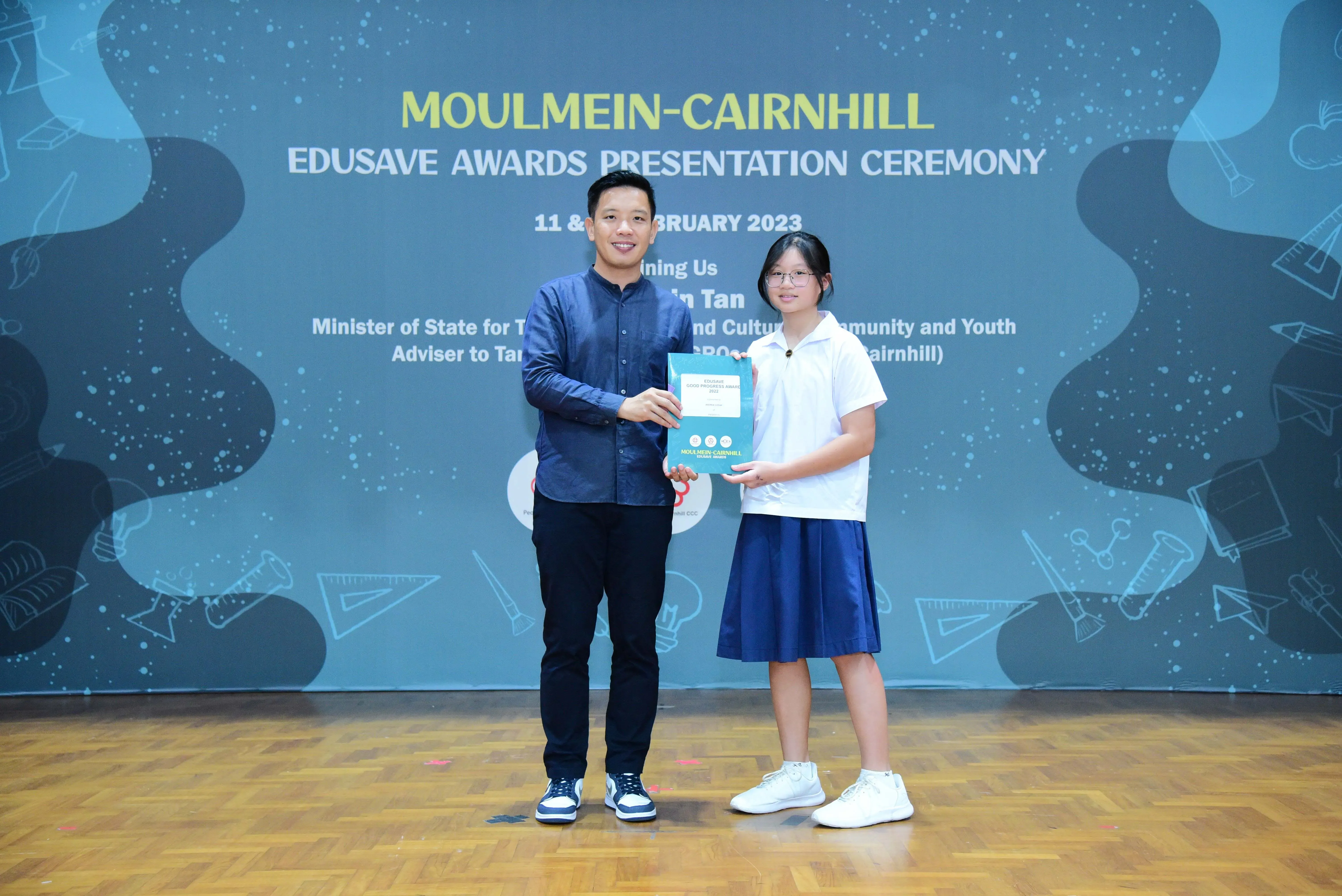 A man and a young girl hold an award together at the Moulmein-Cairnhill Edusave Awards Presentation Ceremony 2023.