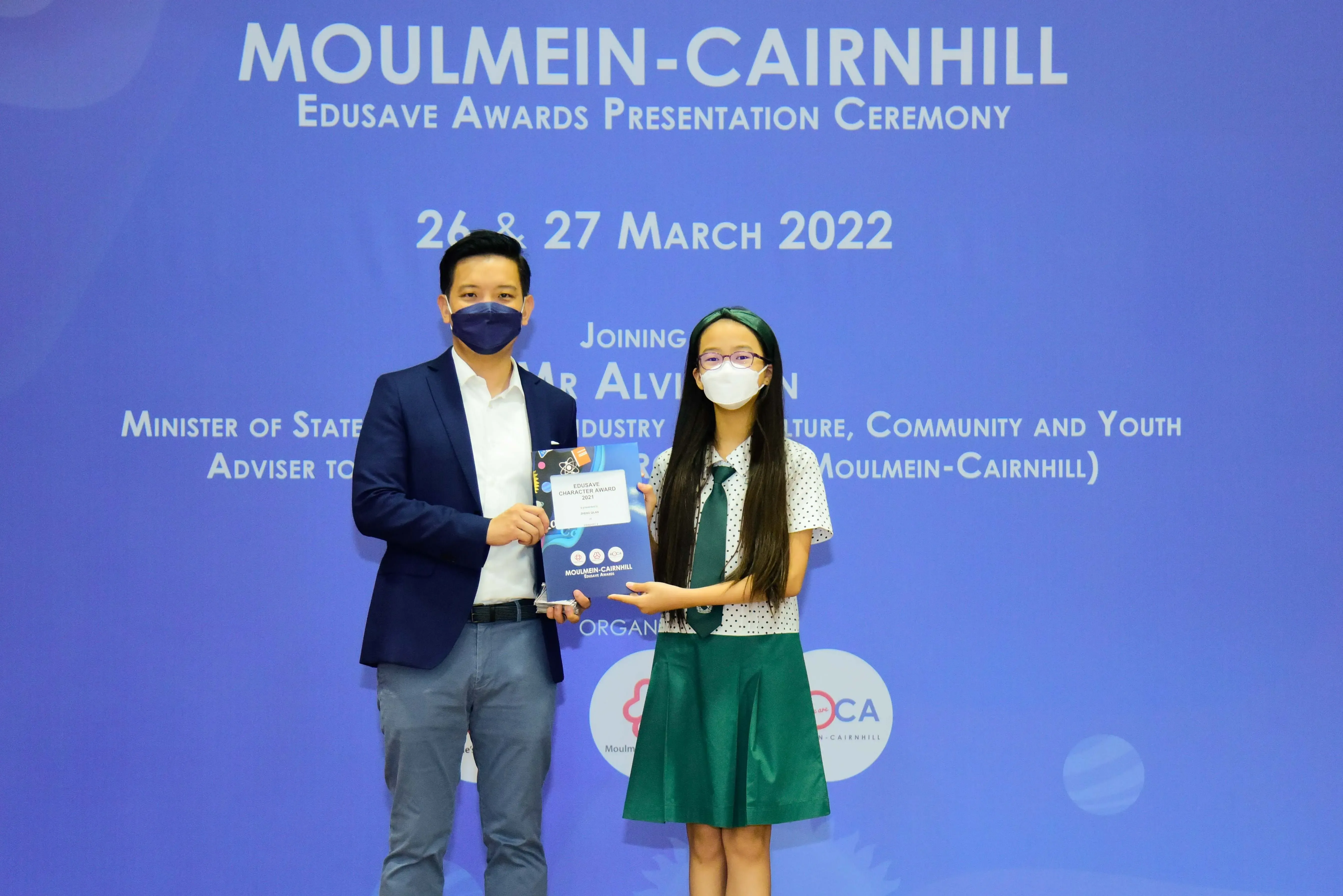 Two masked people hold an award at the Moulmein-Cairnhill Edusave Awards Presentation Ceremony on March 26-27, 2022.