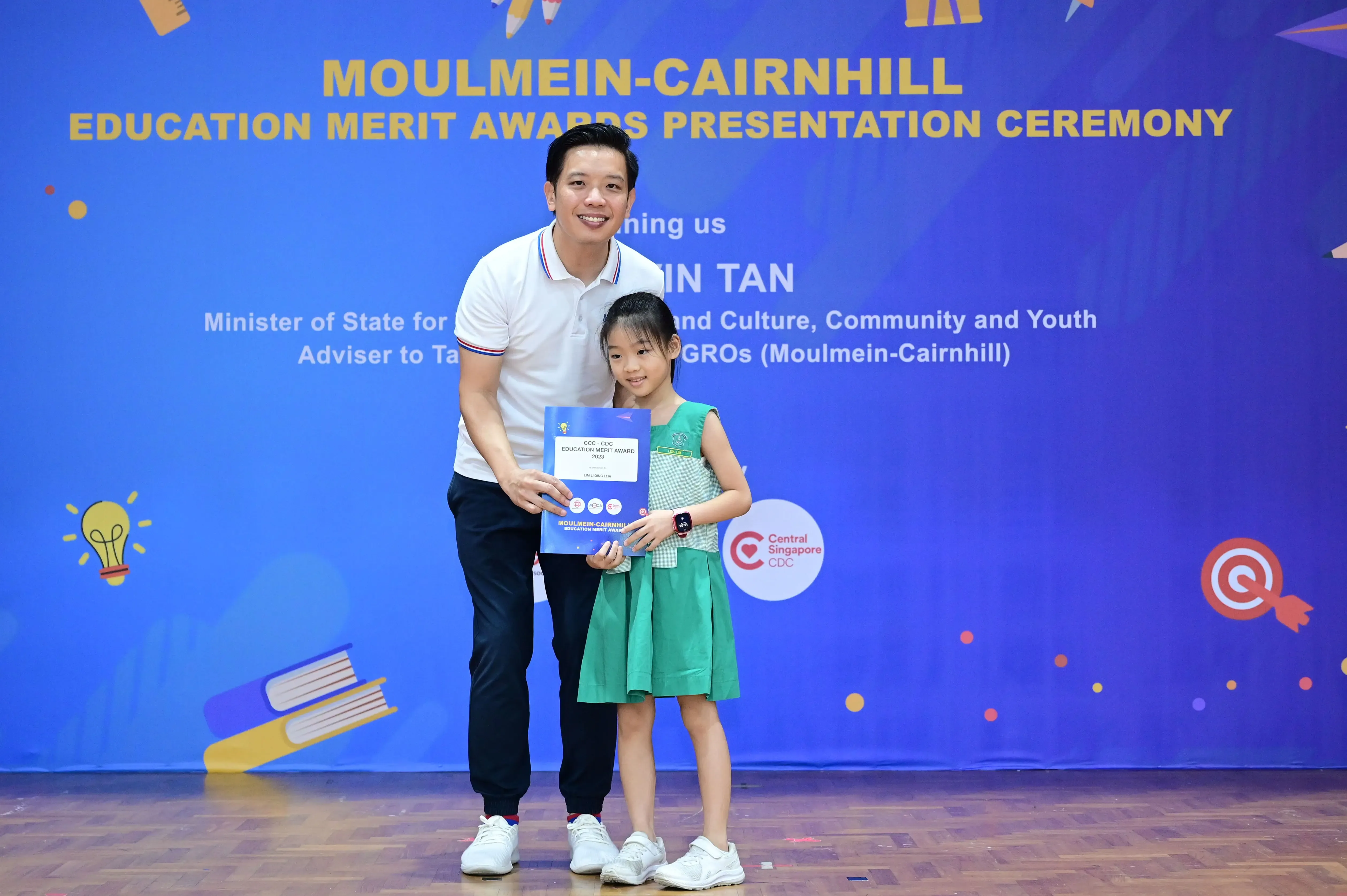 A man and a young girl hold a certificate at the Moulmein-Cairnhill Education Merit Awards Presentation Ceremony.