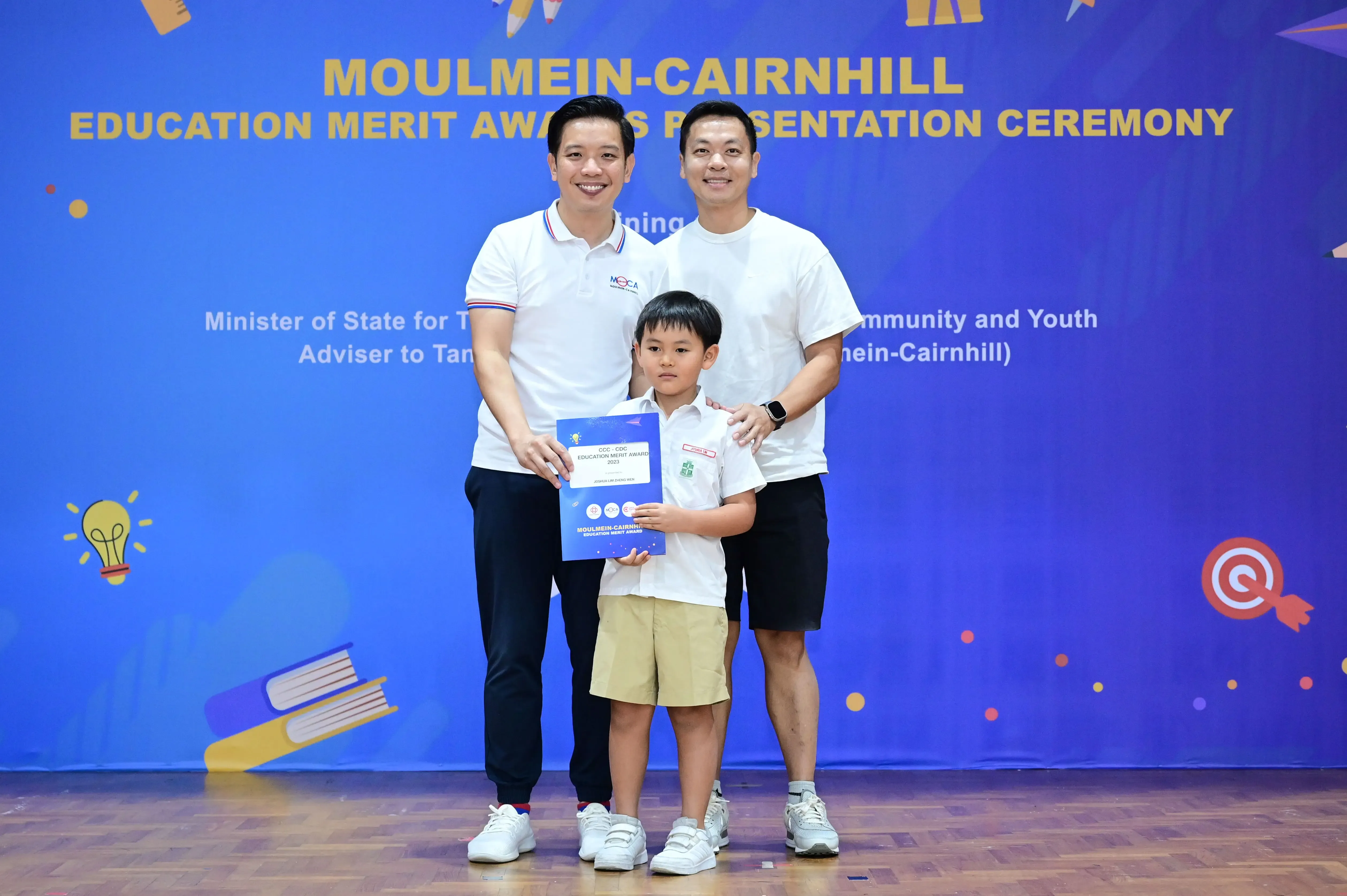 Two men and a young boy hold a certificate at the Moulmein-Cairnhill Education Merit Awards Presentation Ceremony.