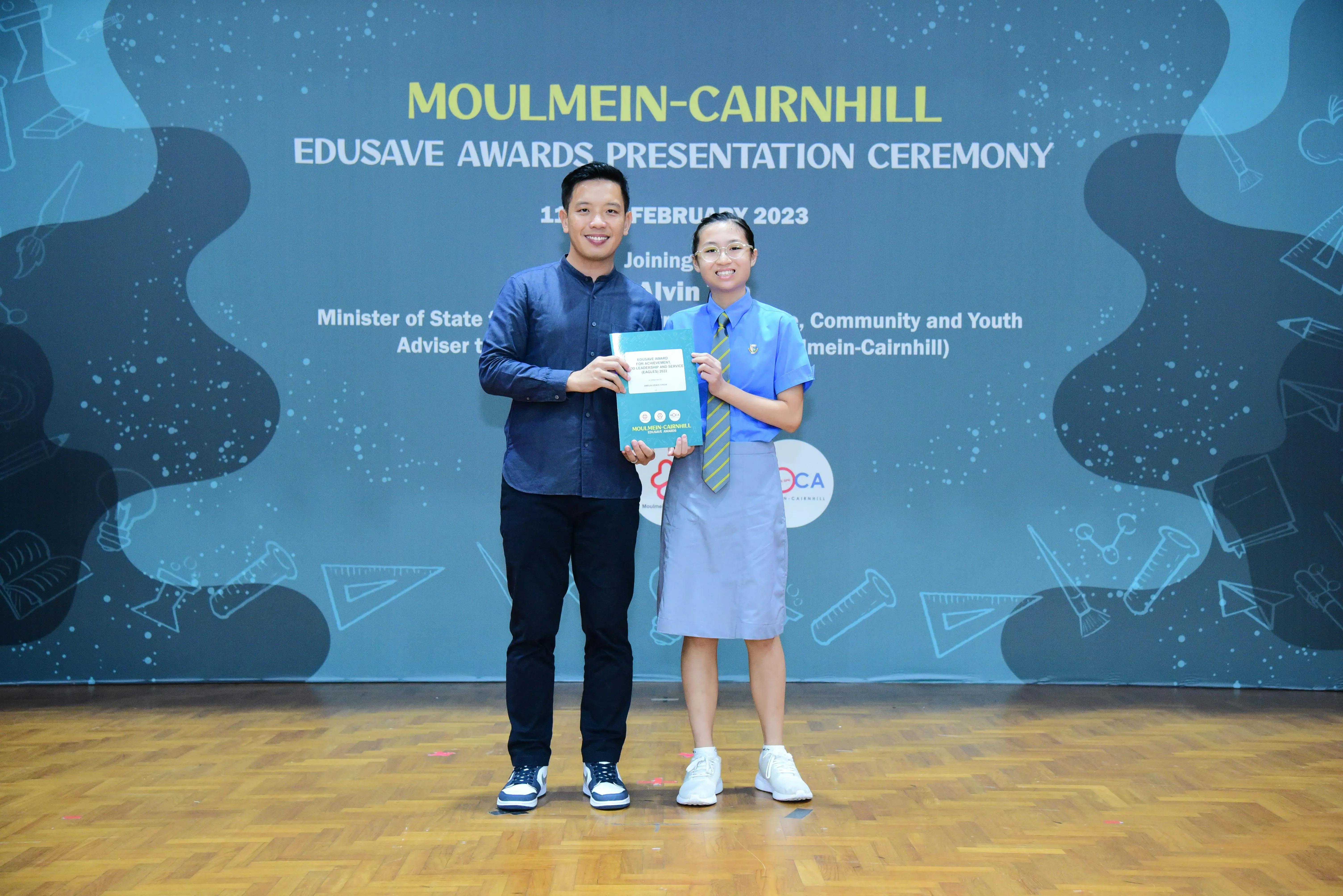Two people hold a booklet at the Moulmein-Cairnhill Edusave Awards Presentation Ceremony in February 2023.