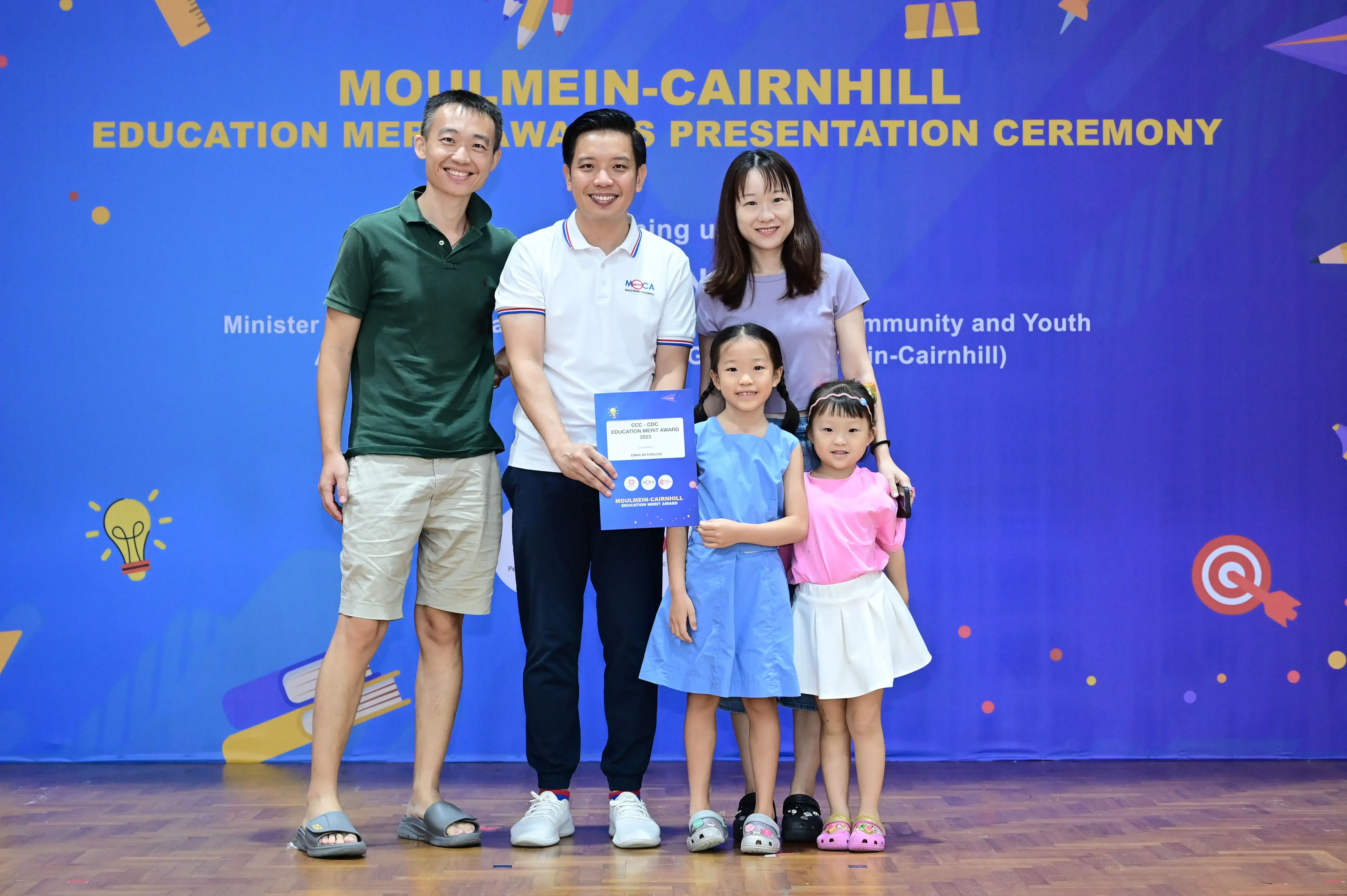 Three adults and two young girls pose with a certificate at the Moulmein-Cairnhill Education Merit Awards Presentation Ceremony.