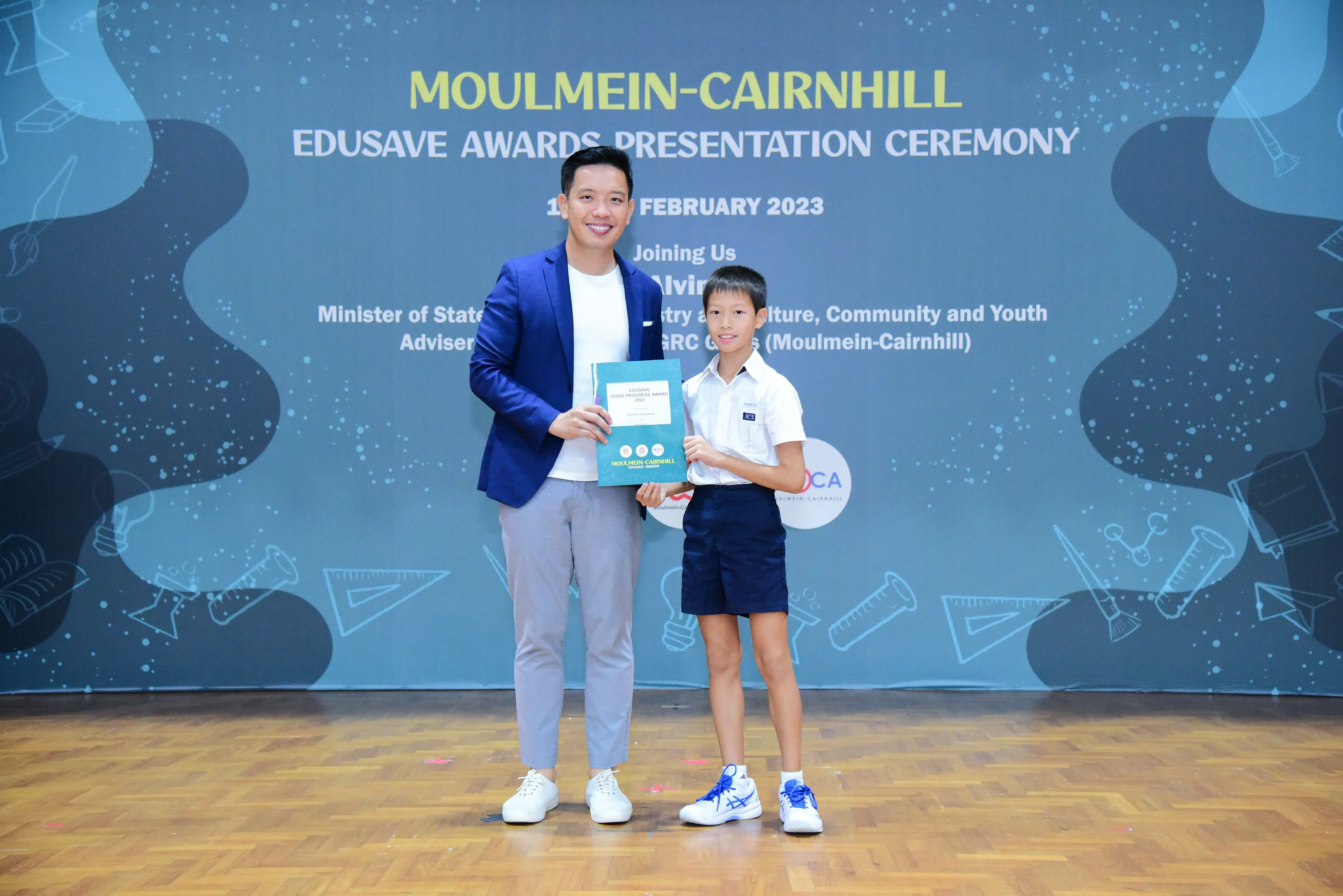 A man in a blue blazer and a young boy in school uniform hold a certificate at the Moulmein-Cairnhill Edusave Awards 2023.