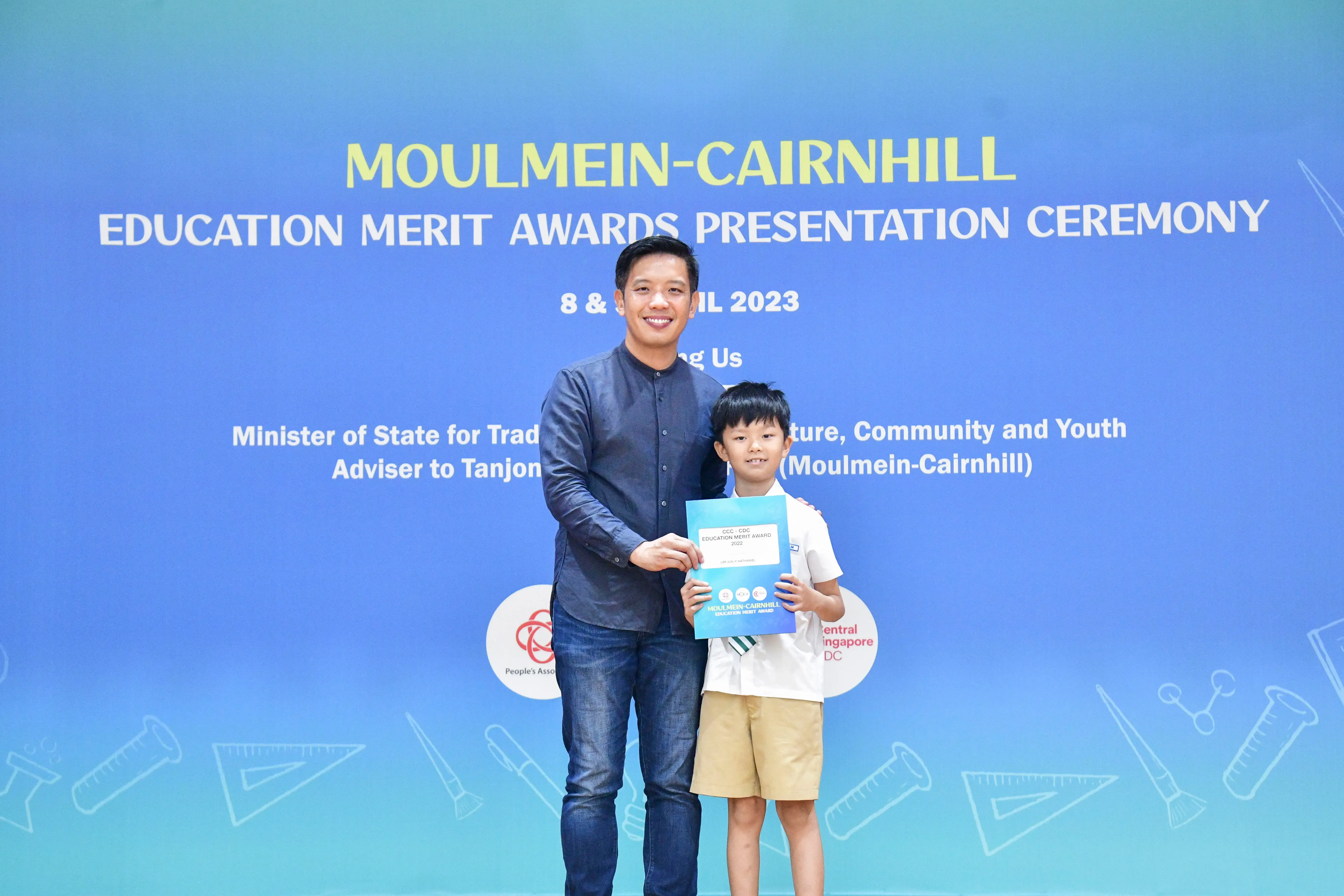 A man and a young boy hold a certificate together at the Moulmein-Cairnhill Education Merit Awards Ceremony 2023.
