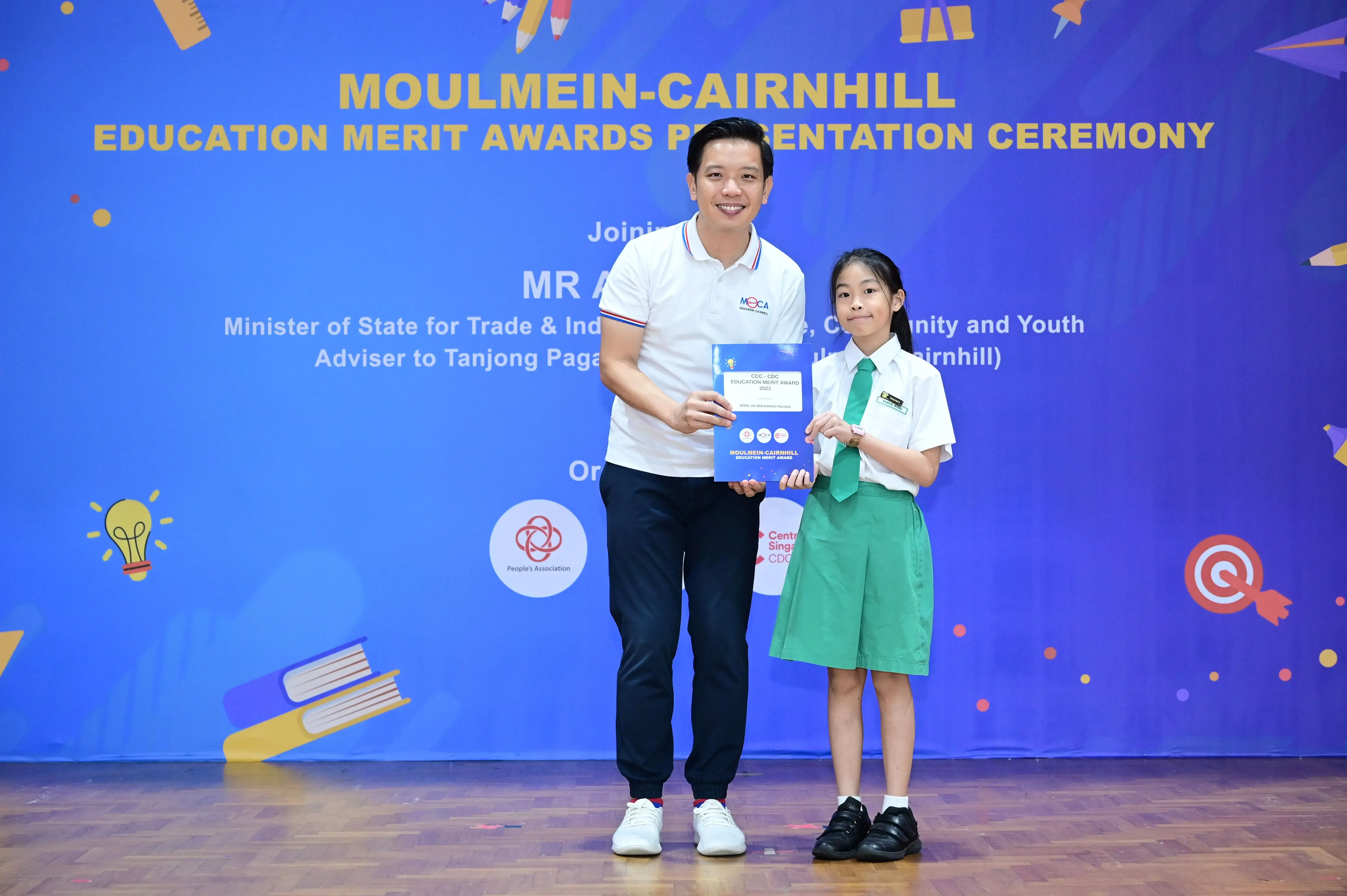 A man and a young girl in school uniform hold an award certificate at the Moulmein-Cairnhill Education Merit Awards ceremony.