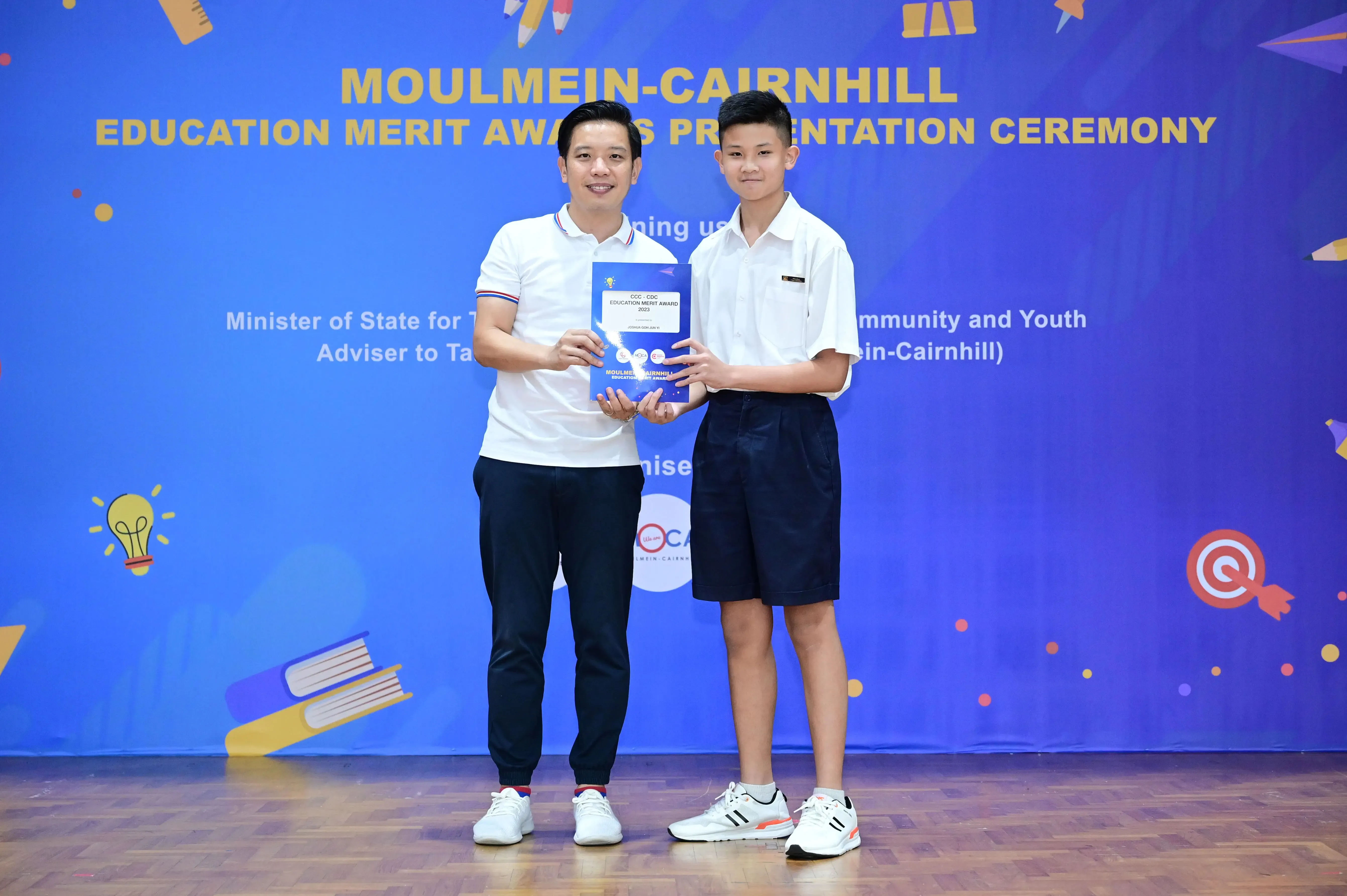 Two people hold an award booklet at the Moulmein-Cairnhill Education Merit Awards Presentation Ceremony.