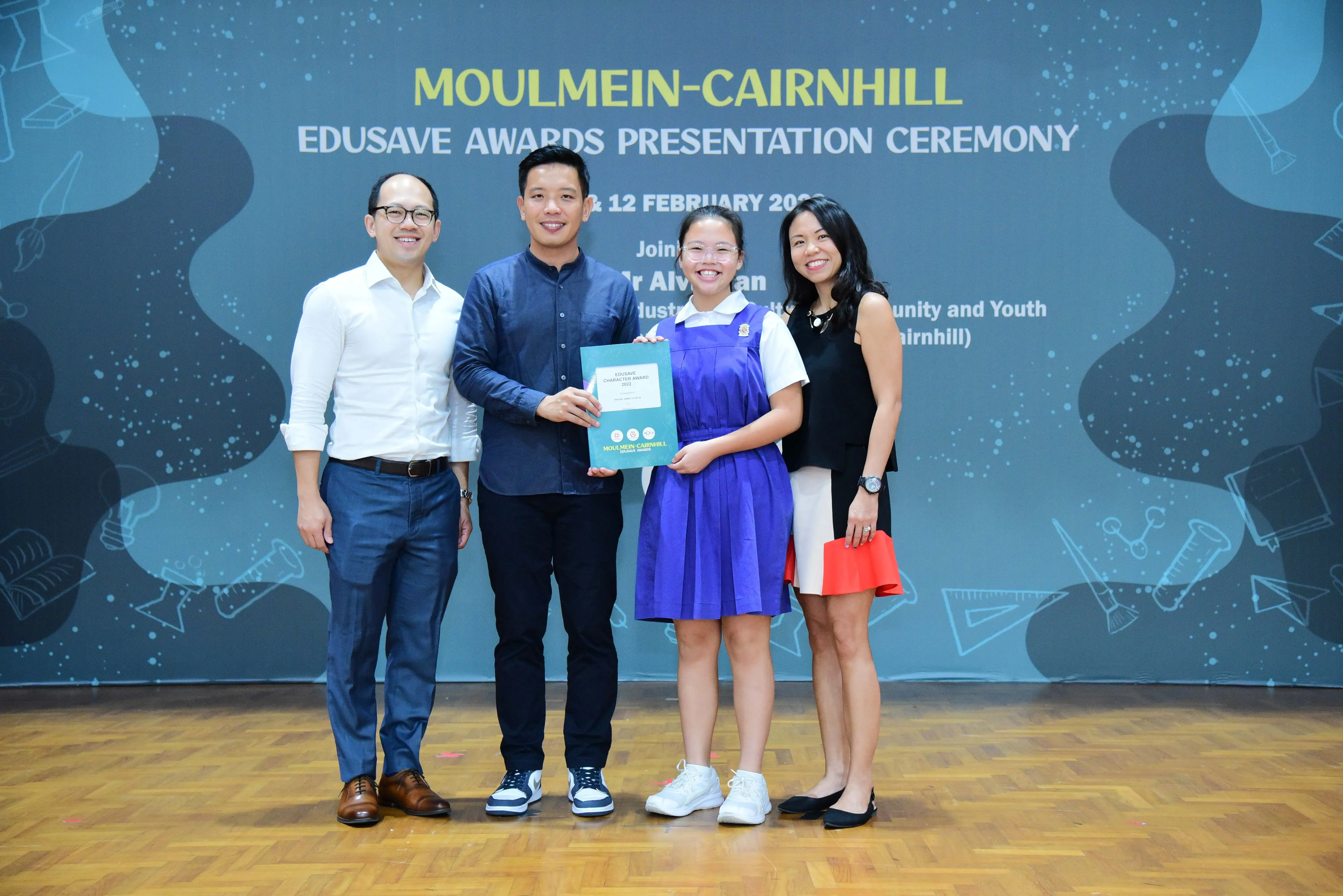 Four people pose at the Moulmein-Cairnhill Edusave Awards Presentation Ceremony, with a student holding a certificate.