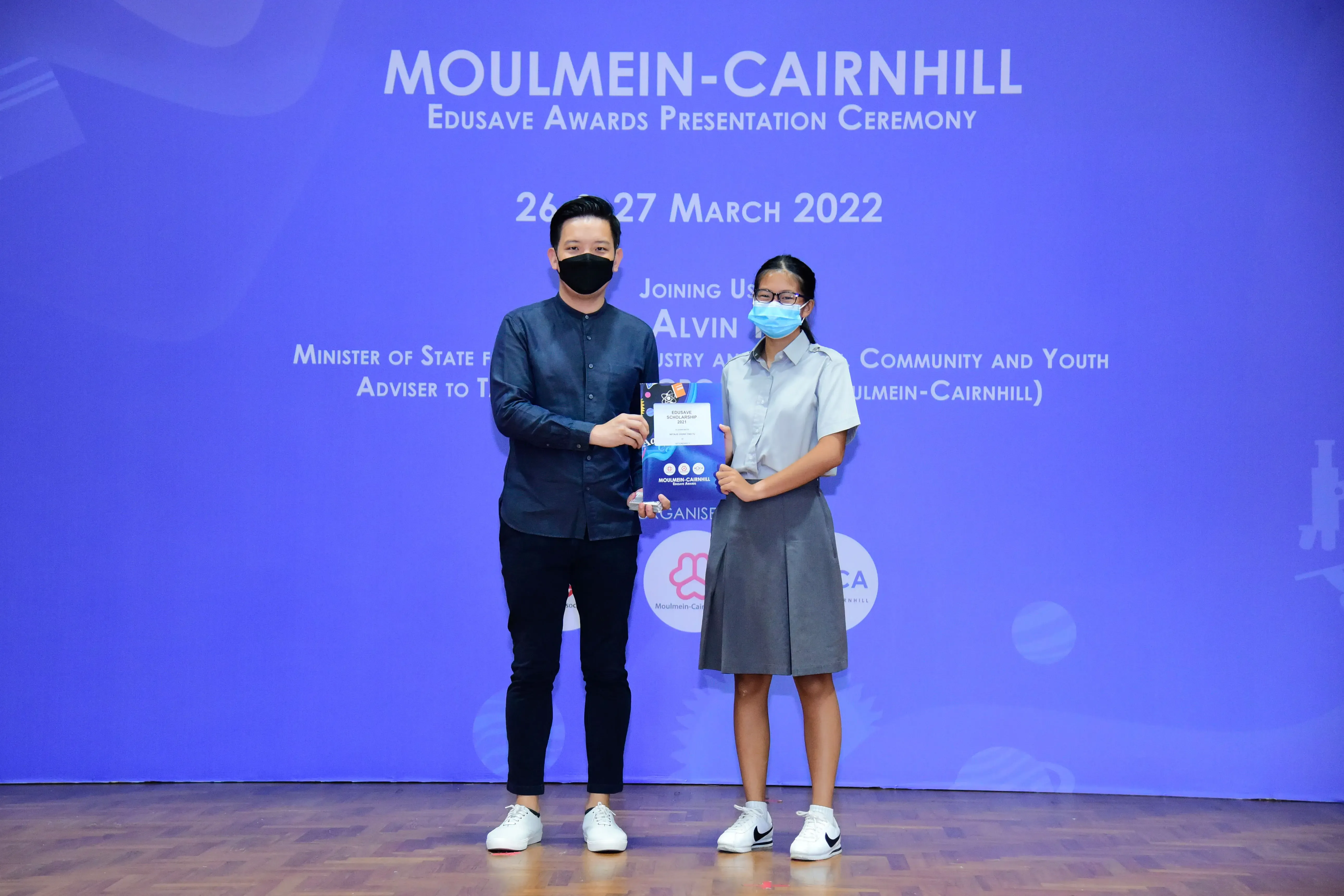 Two masked people hold a certificate at the Moulmein-Cairnhill Edusave Awards Presentation Ceremony, March 2022.