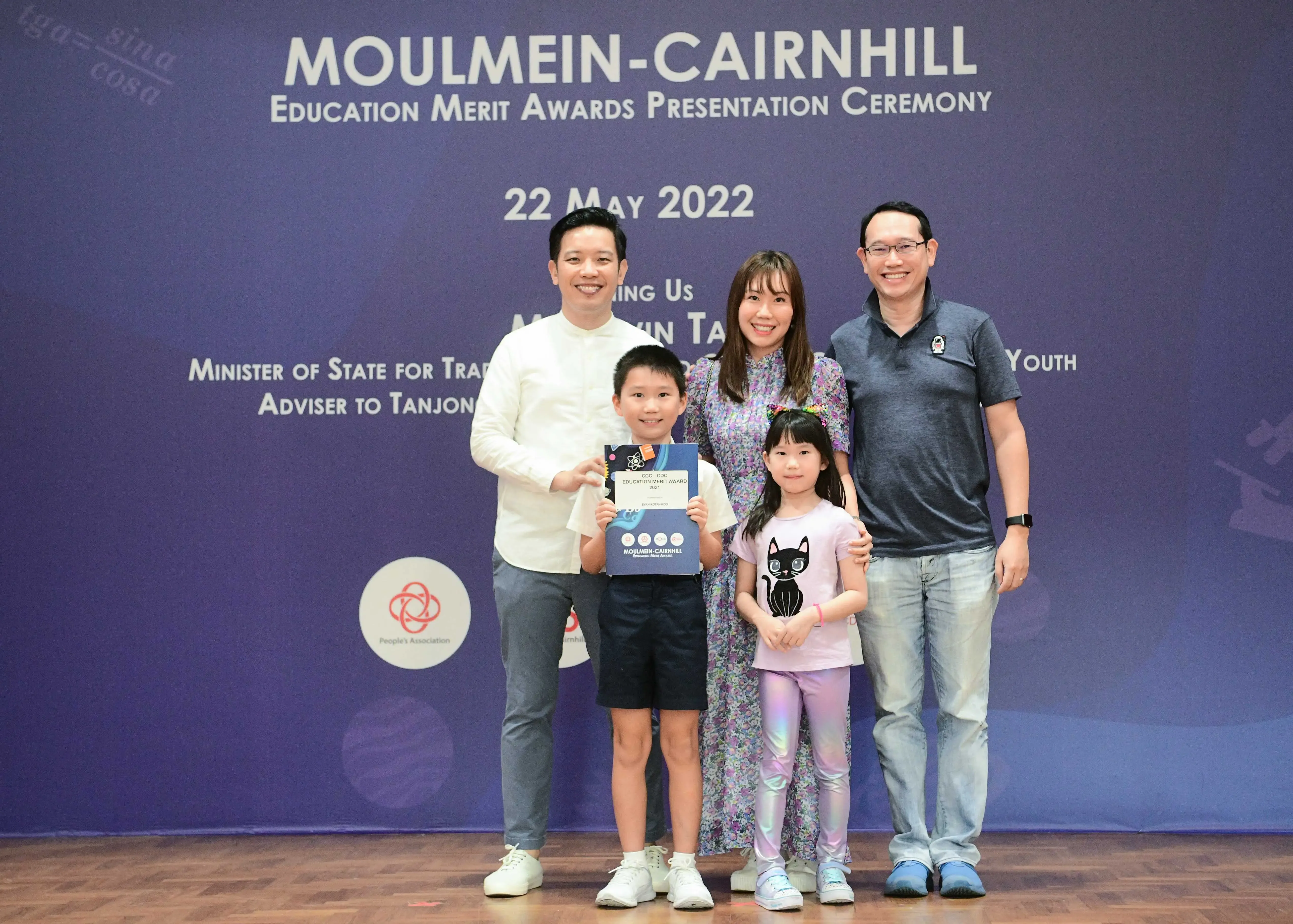 Five people pose at the Moulmein-Cairnhill Education Merit Awards Ceremony on 22 May 2022, with a boy holding an award.