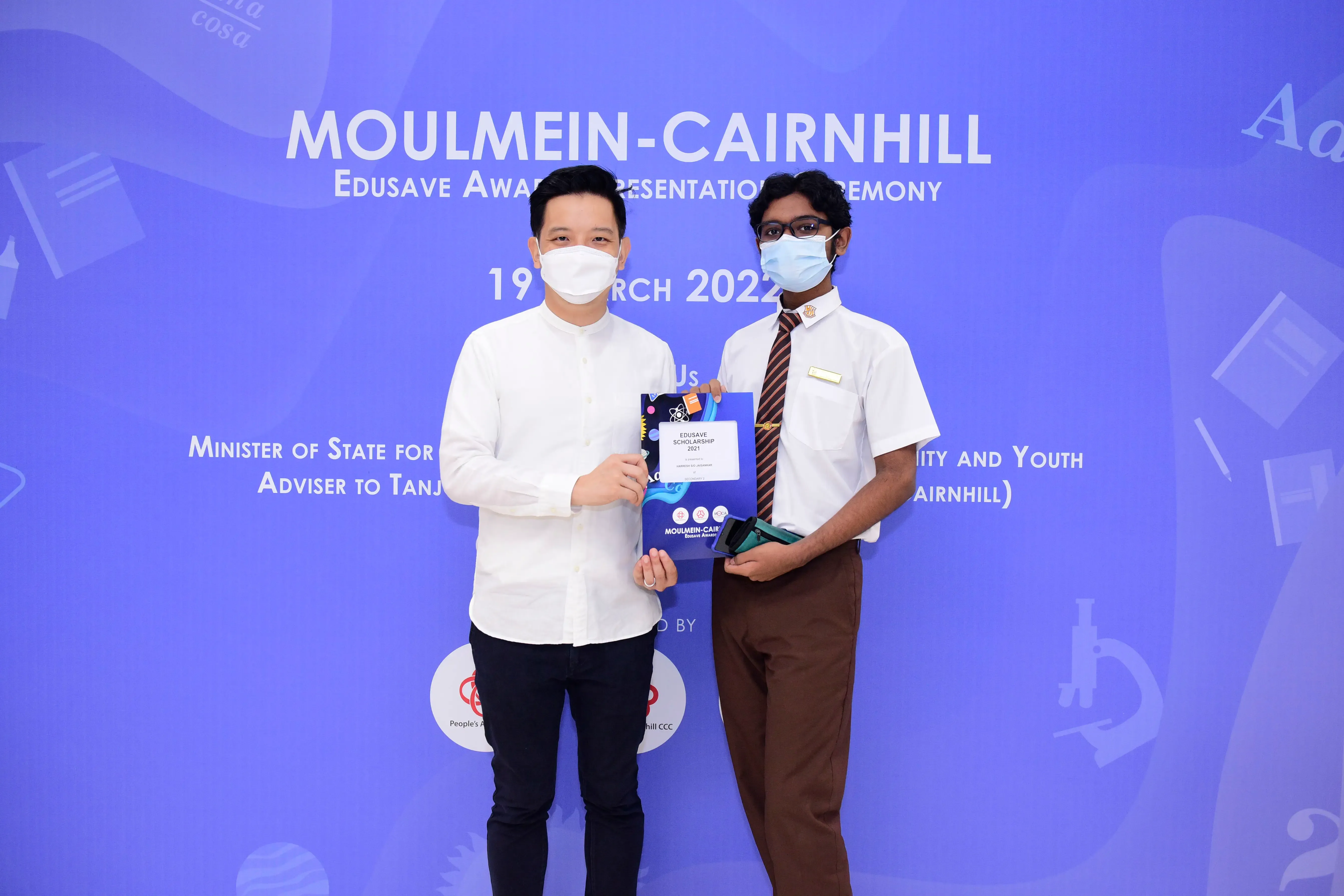 Two masked men hold an Edusave Scholarship certificate at the Moulmein-Cairnhill Awards Ceremony on 19 March 2022.