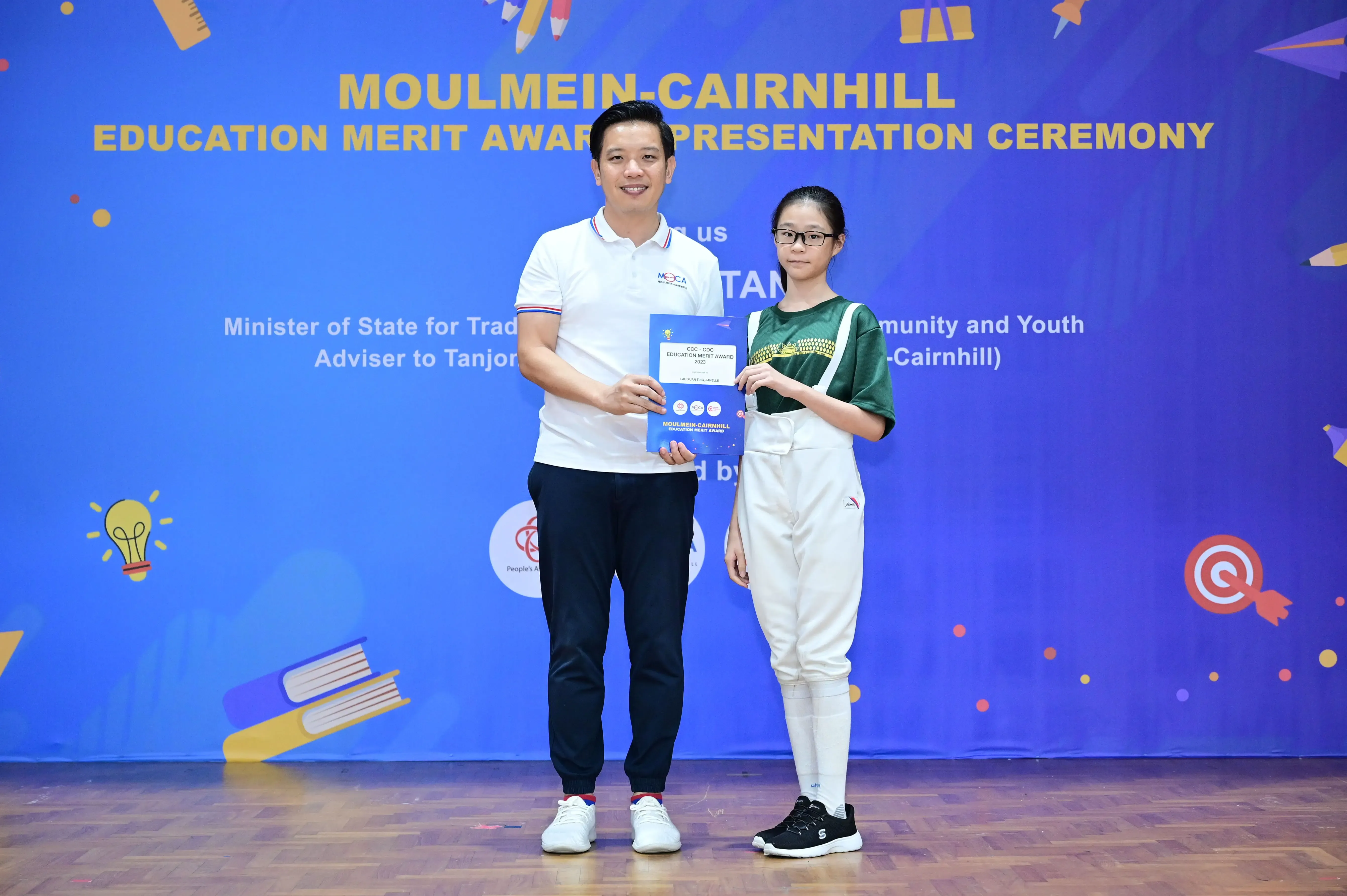 A man and a young girl hold an award certificate at the Moulmein-Cairnhill Education Merit Award Presentation Ceremony.