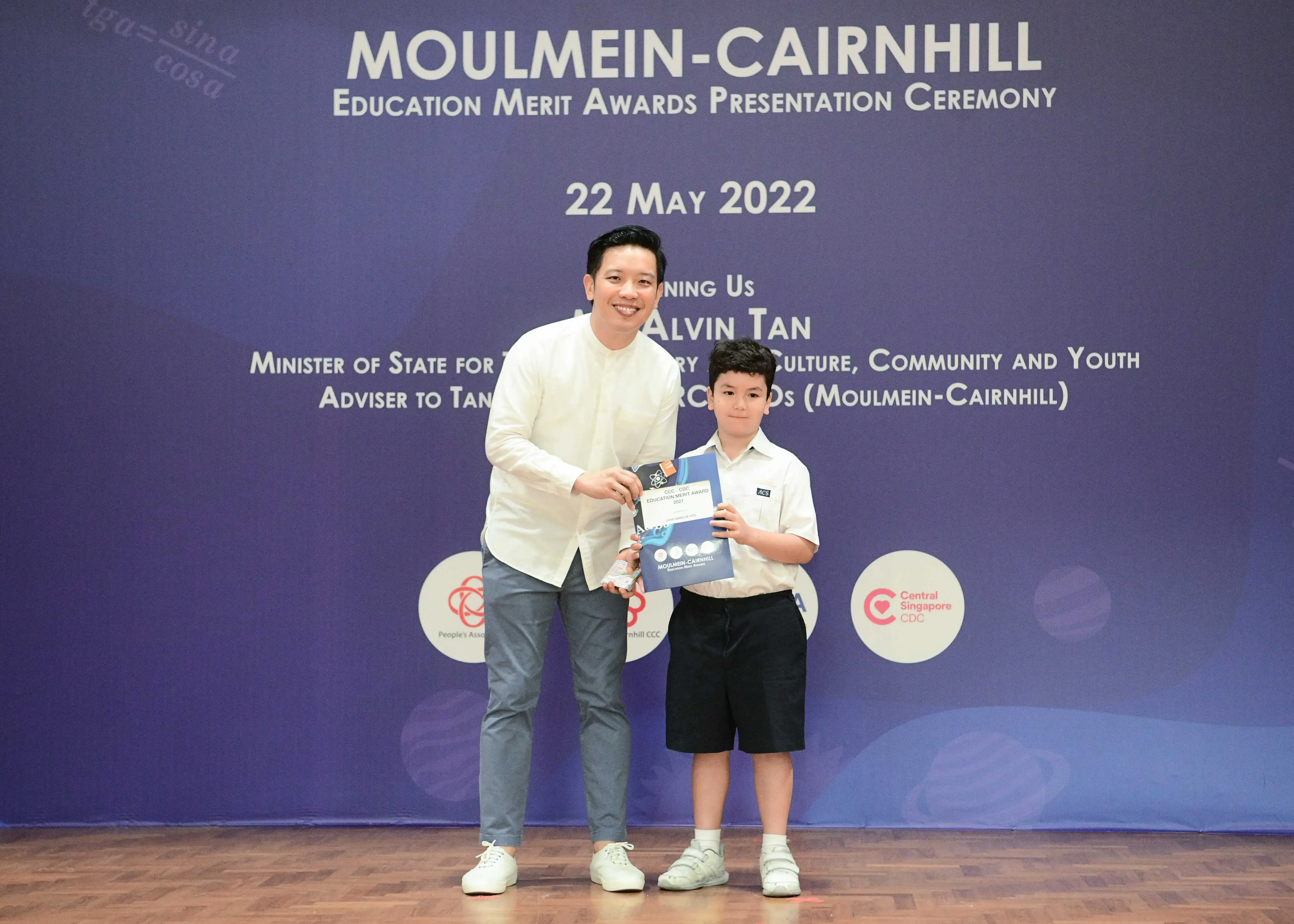An adult and a young boy hold an award certificate at the Moulmein-Cairnhill Education Merit Awards on 22 May 2022.