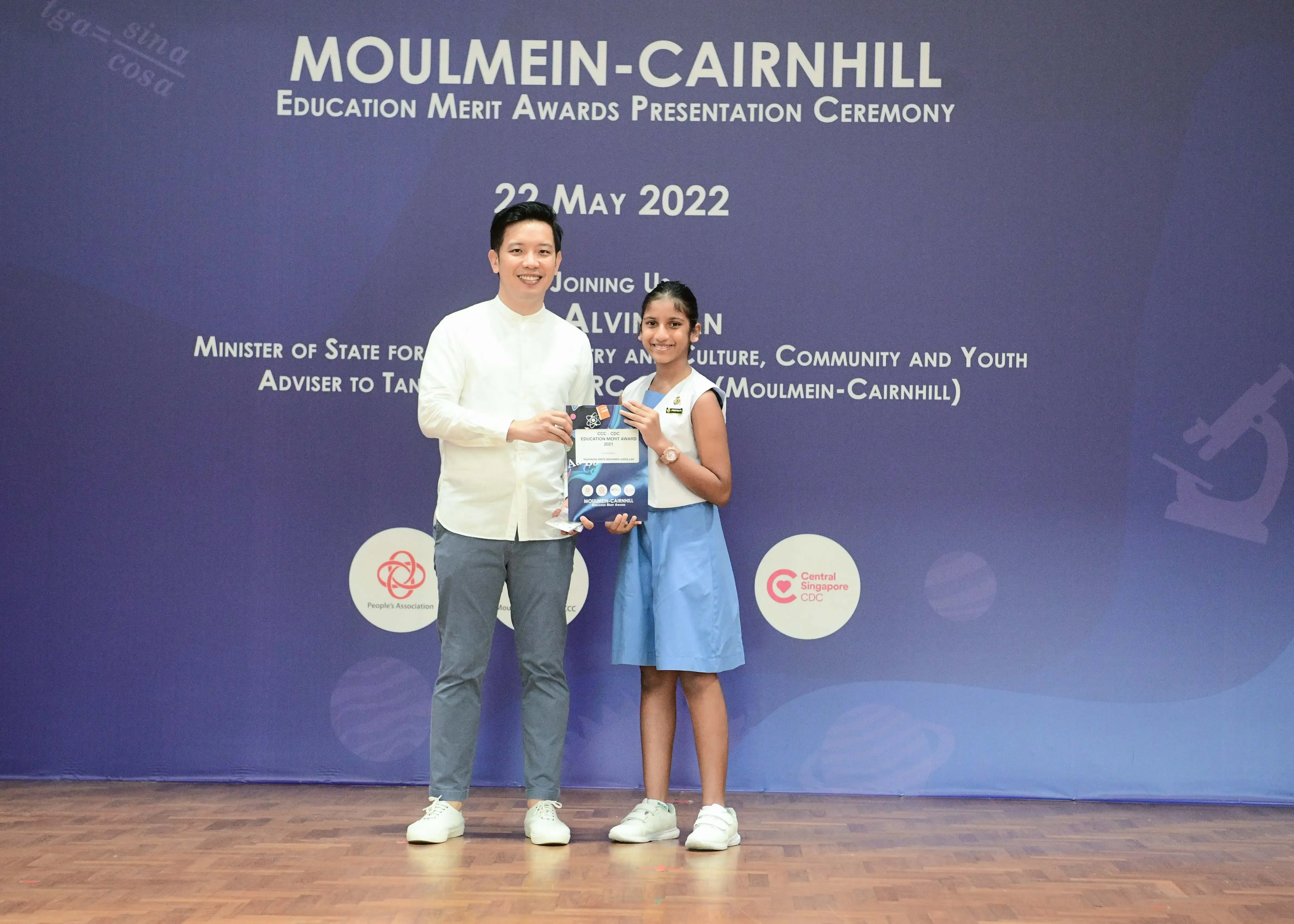 A man and a young girl hold an award together at the Moulmein-Cairnhill Education Merit Awards Ceremony on 22 May 2022.