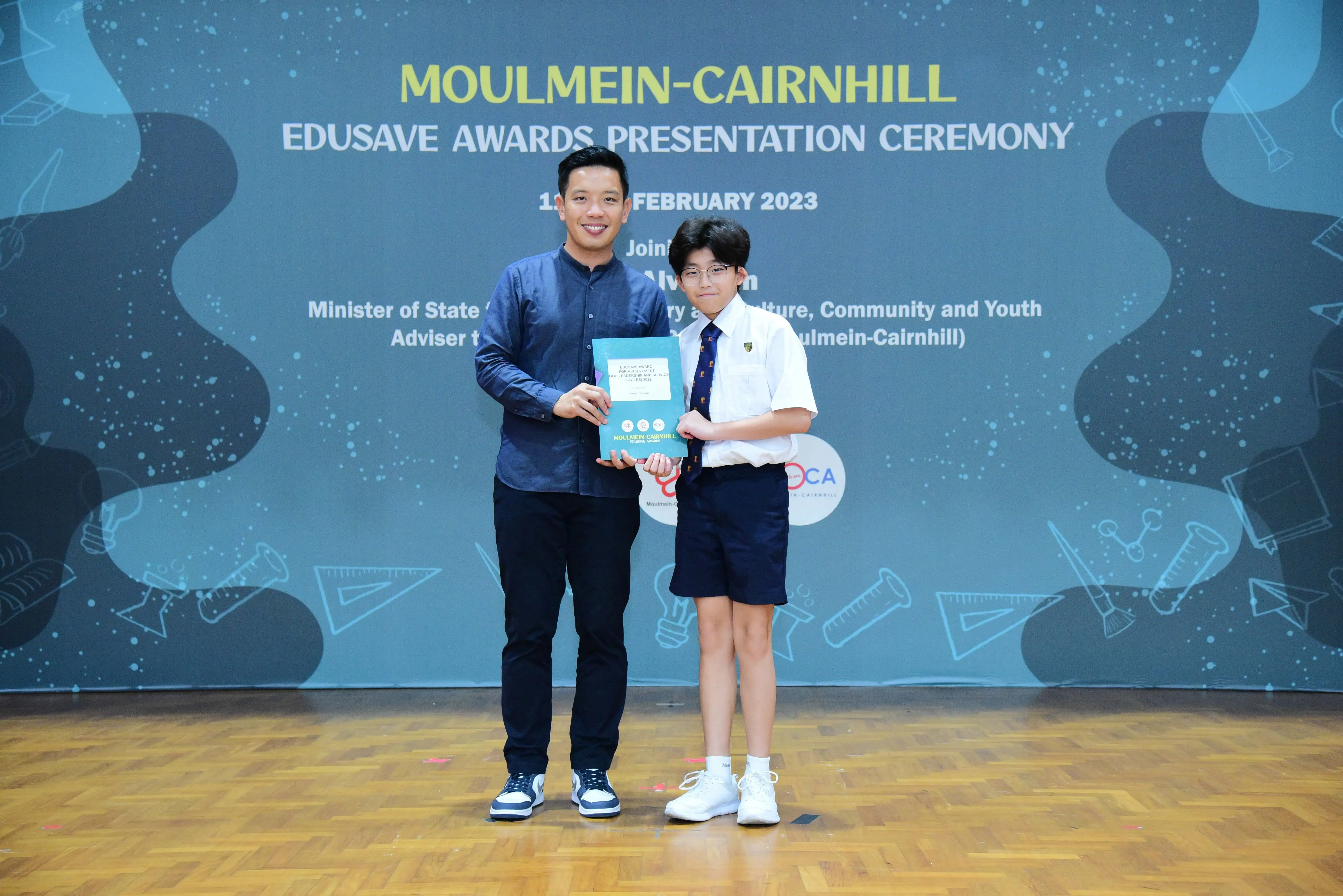 An adult and a uniformed student hold an award together at the Moulmein-Cairnhill Edusave Awards Ceremony, February 2023.