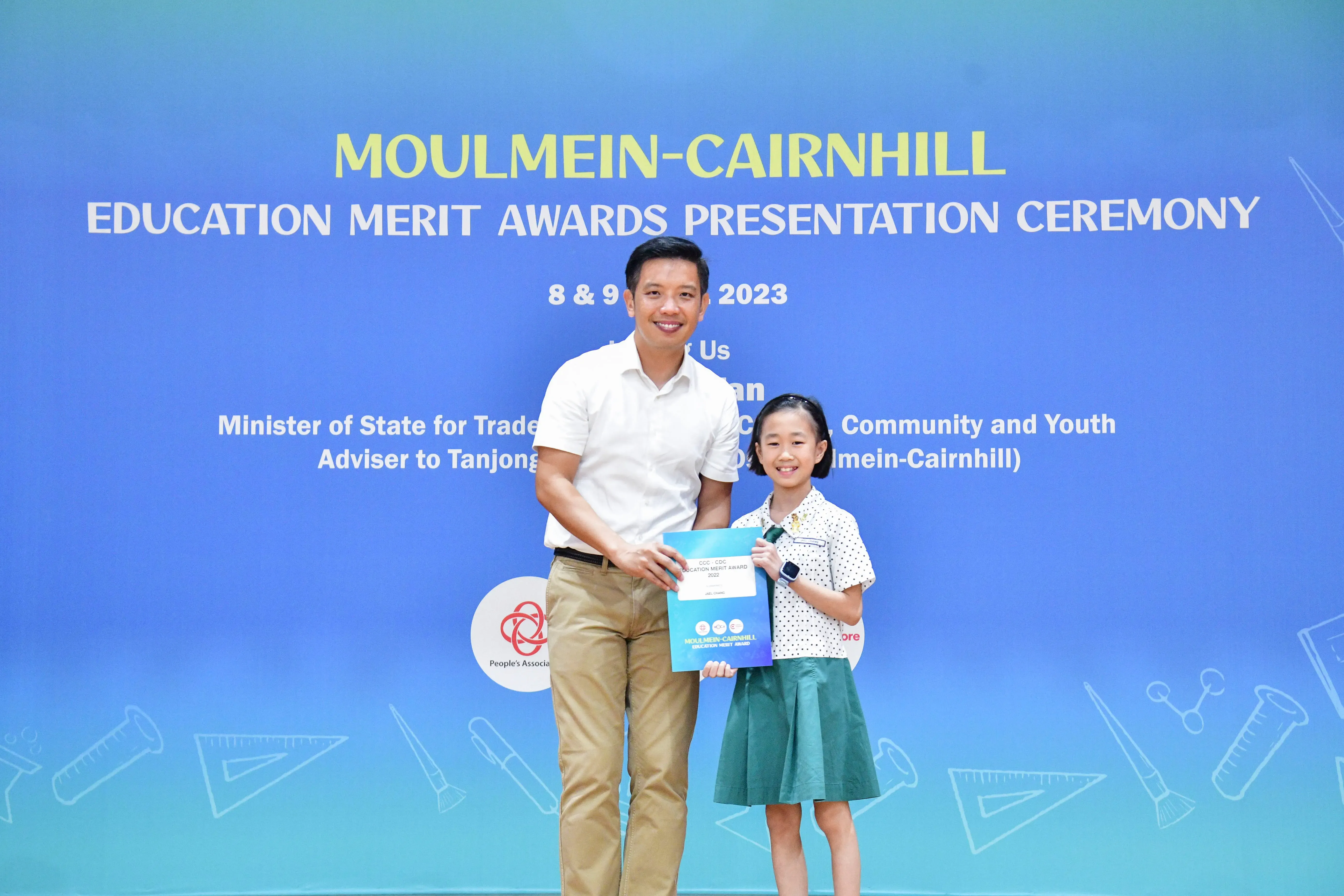 A man and a young girl hold an award certificate at the Moulmein-Cairnhill Education Merit Awards Ceremony 2023.