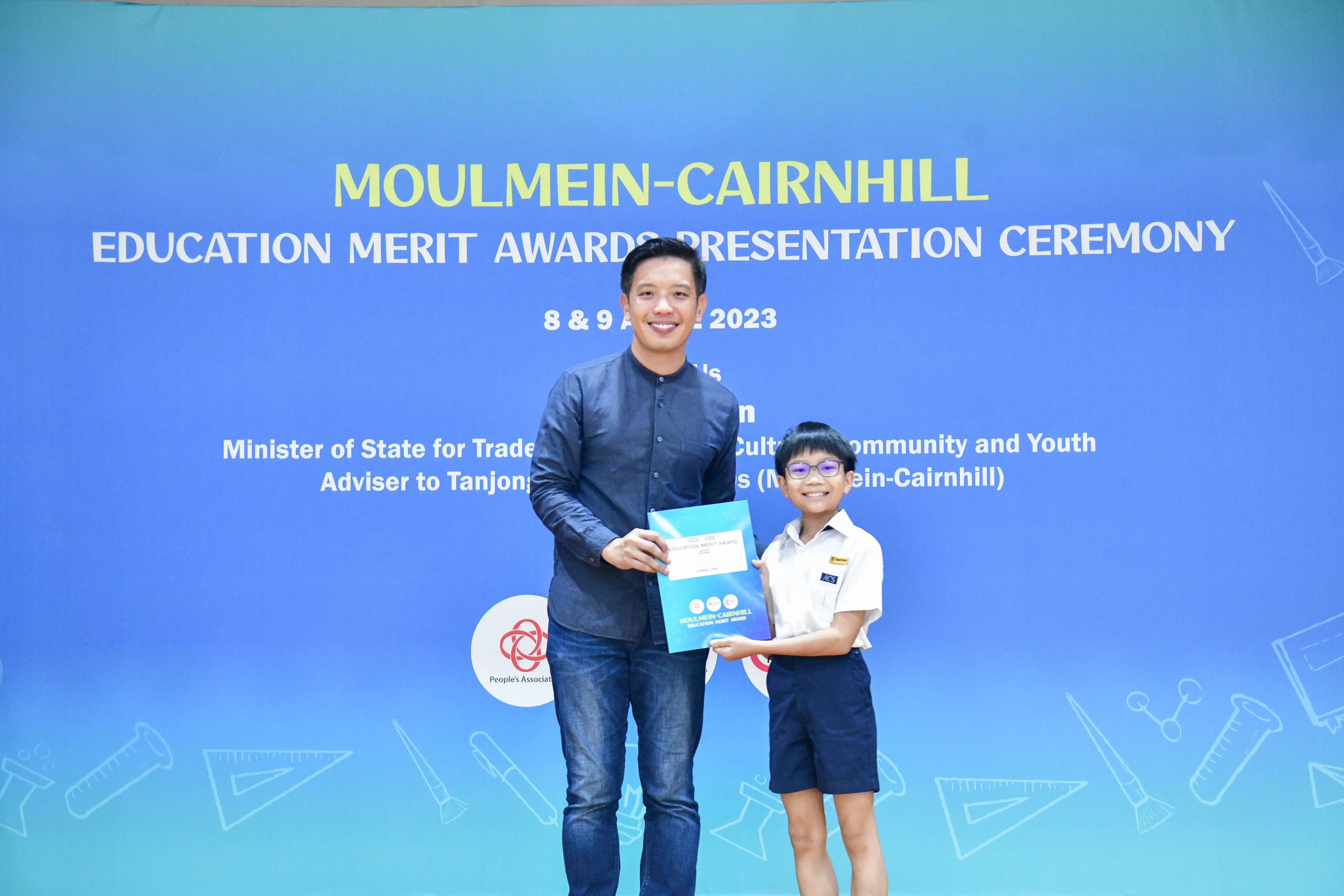 A man and a young boy in school uniform hold an award folder at the Moulmein-Cairnhill Education Merit Awards 2023.