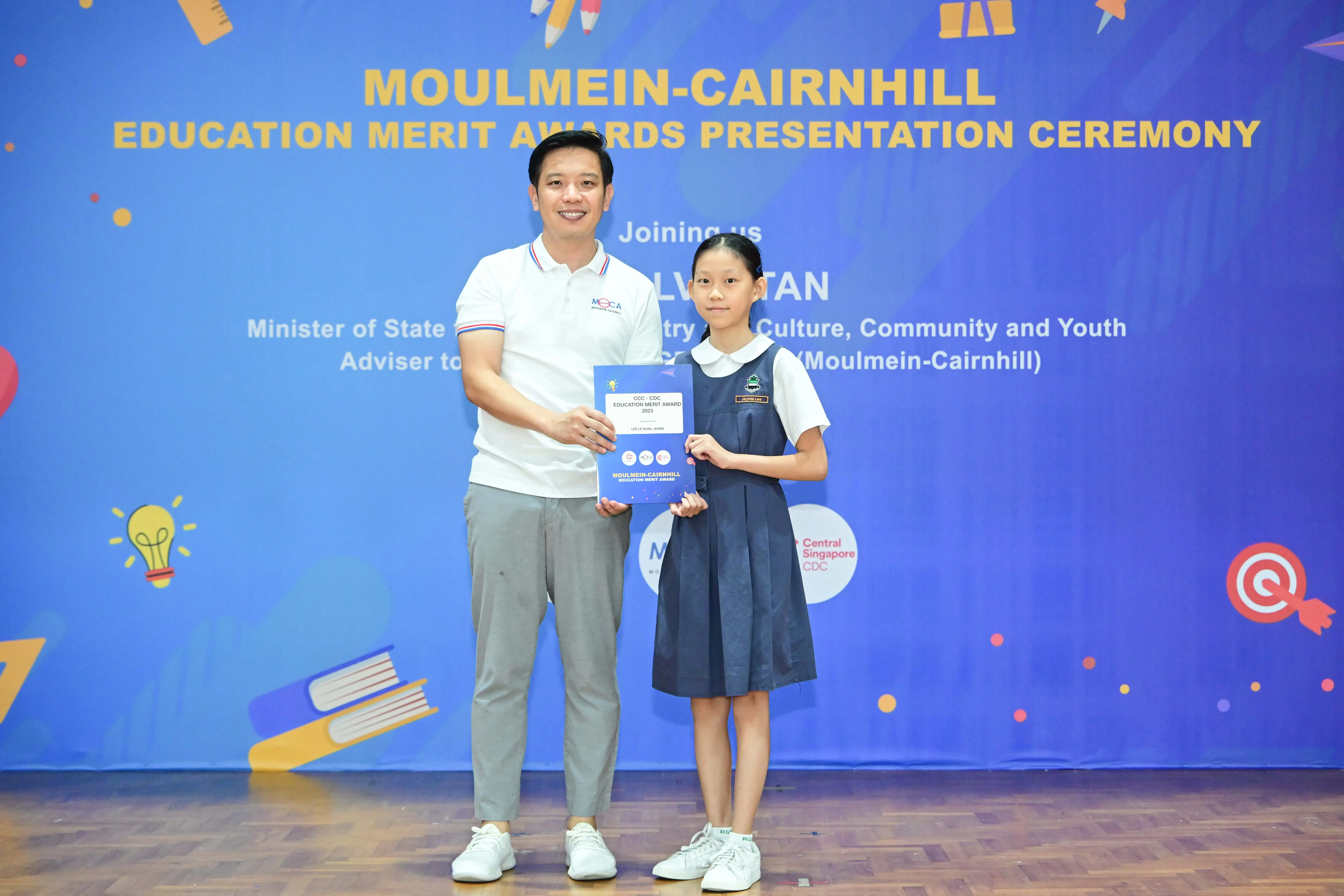 A man and a young girl in school uniform hold a certificate at the Moulmein-Cairnhill Education Merit Awards ceremony.