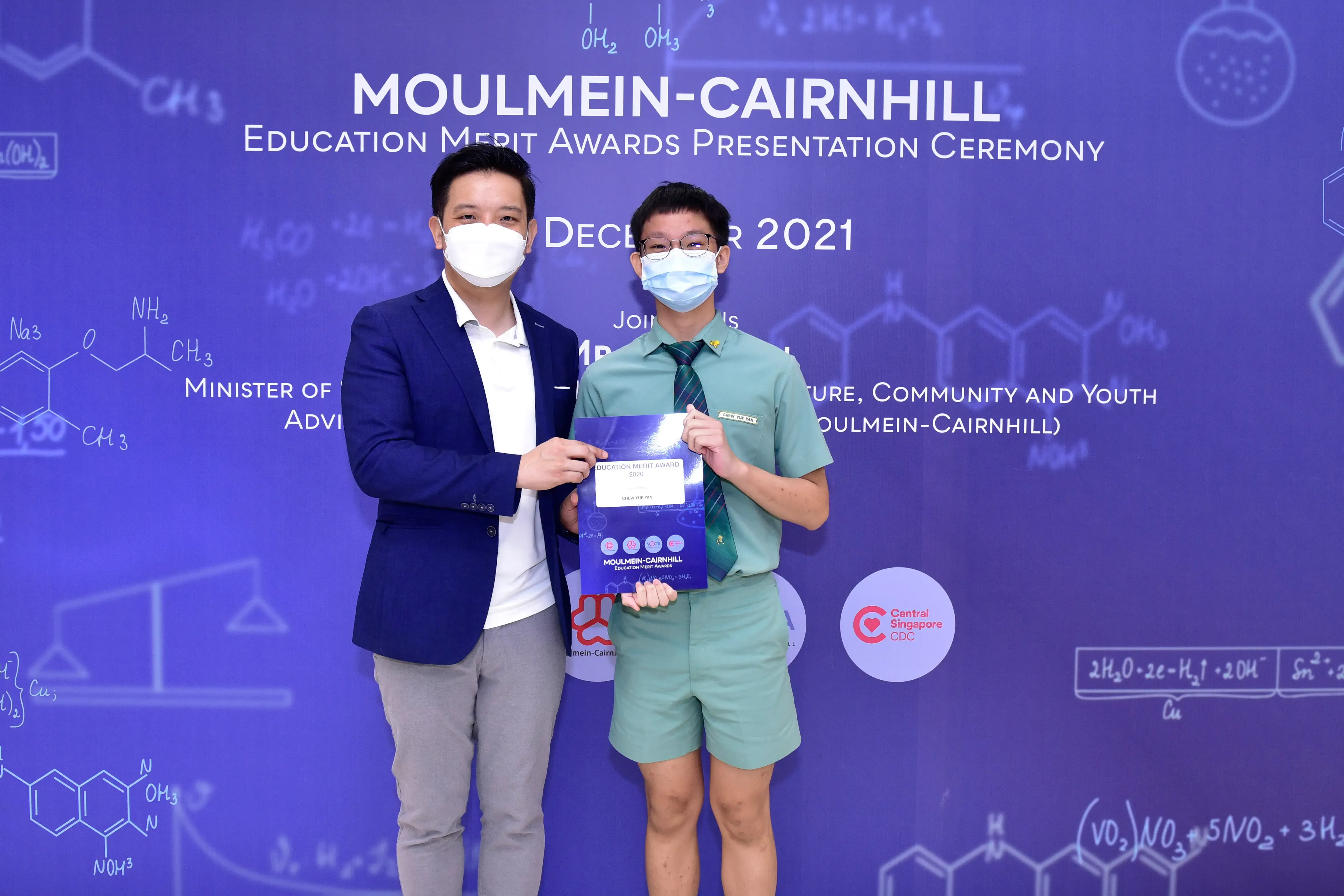 Two masked people hold an award certificate at the Moulmein-Cairnhill Education Merit Awards Ceremony, December 2021.