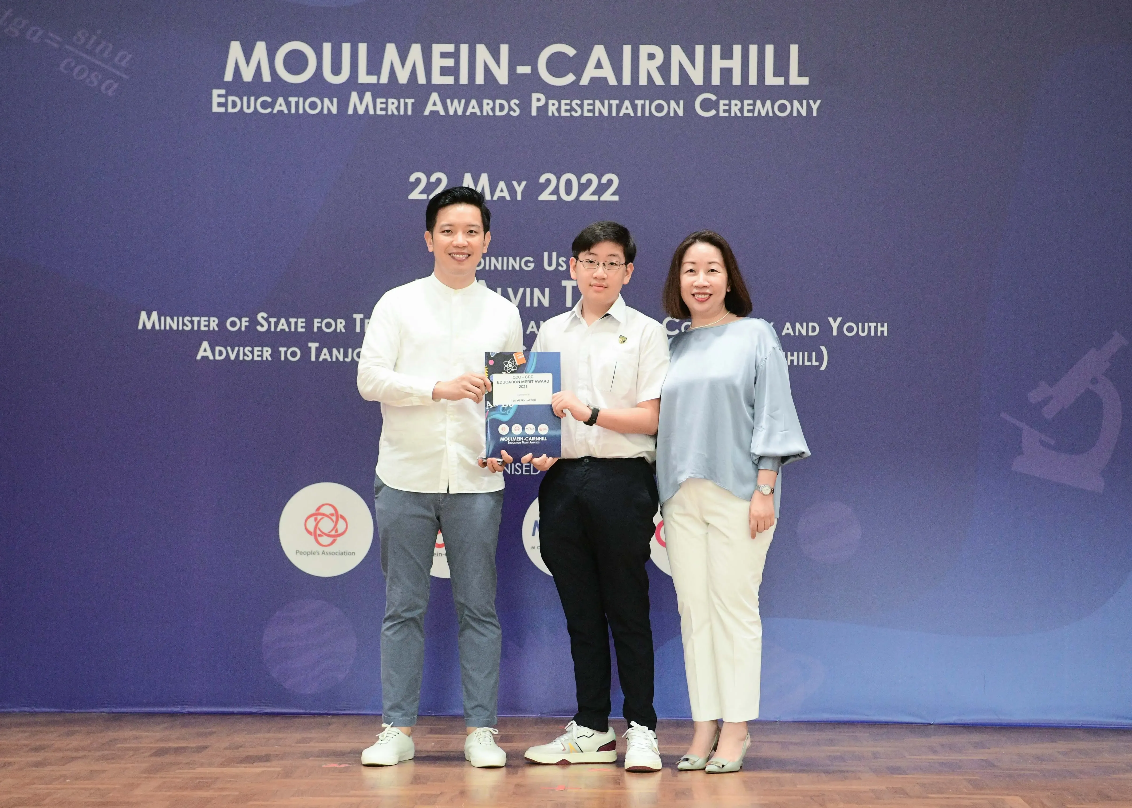 Three people pose on stage at the Moulmein-Cairnhill Education Merit Awards Presentation Ceremony on 22 May 2022.